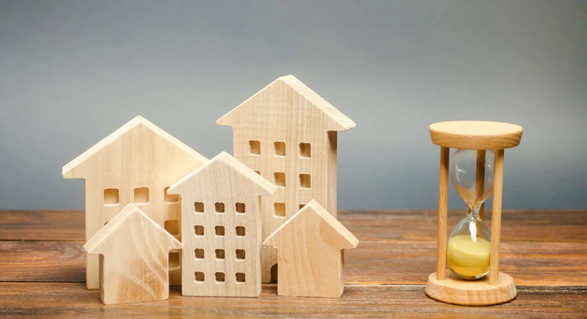Prazos do crédito habitação: Conhece os novos limites? casas de madeira e uma ampulheta sobre a mesa a representar os novos prazos do crédito habitação