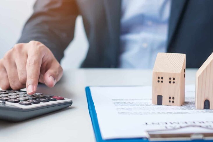 Senhor com calculadora, contrato e duas casas de brincar em cima de mesa