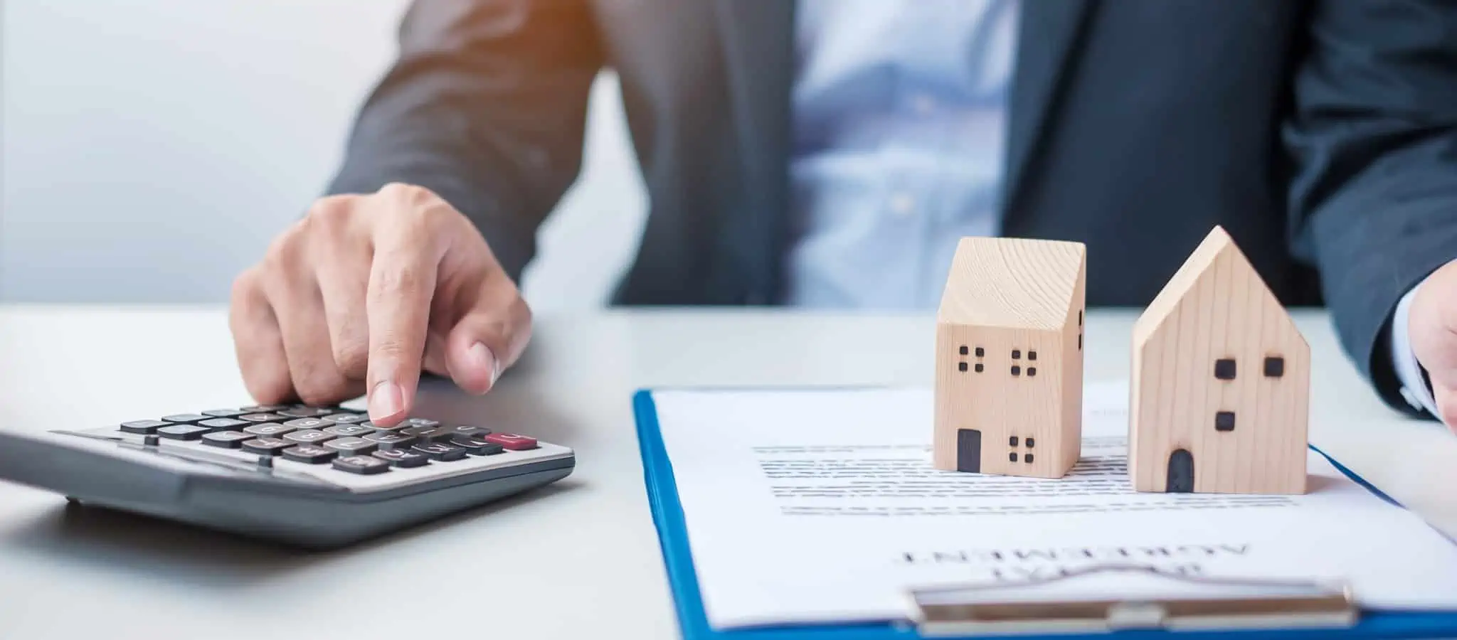 Senhor com calculadora, contrato e duas casas de brincar em cima de mesa