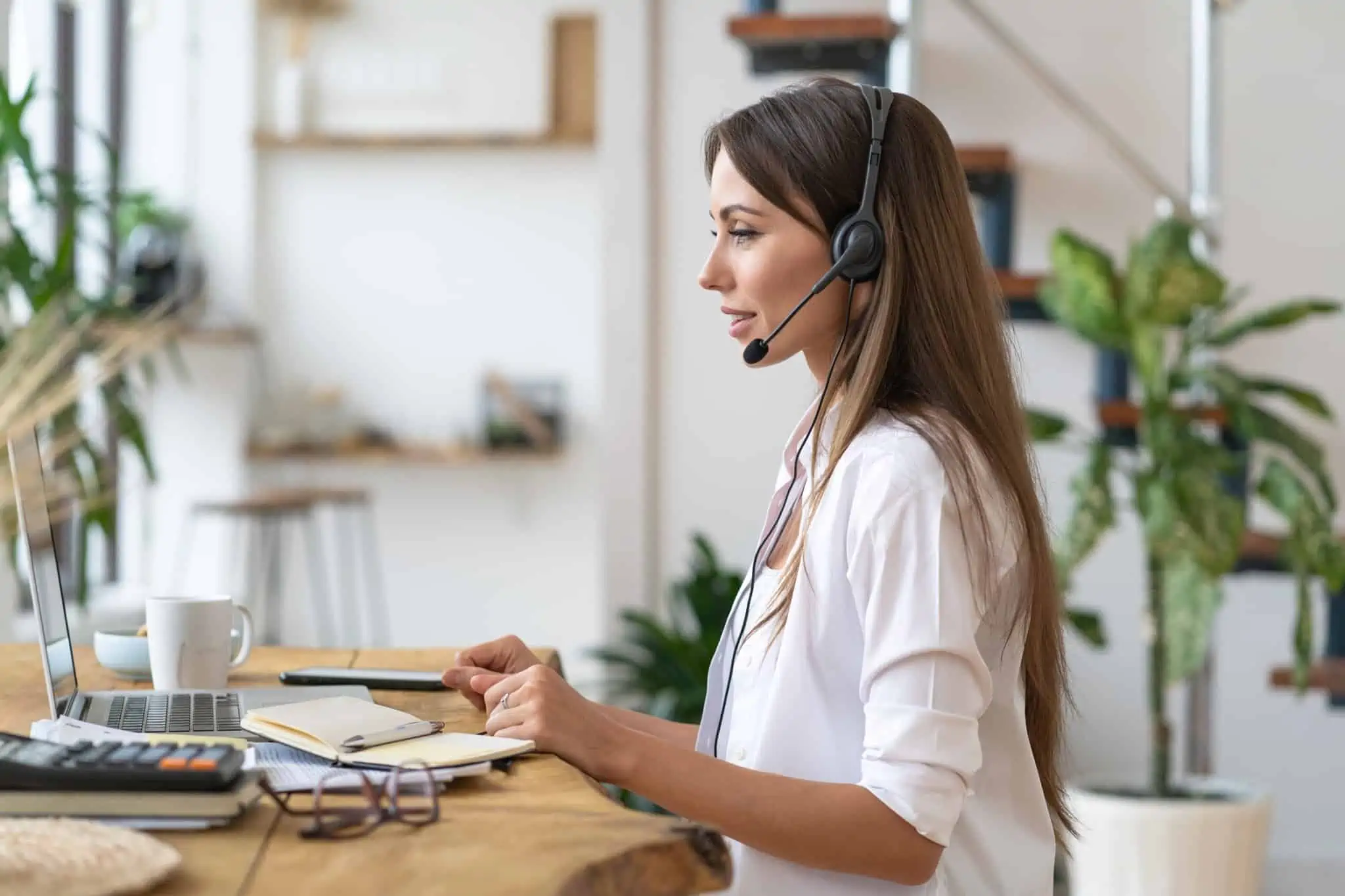 Teletrabalho: O que é considerado local de trabalho? jovem mulher a trabalhar em casa, em teletrabalho, a falar com phones e a usar o computador