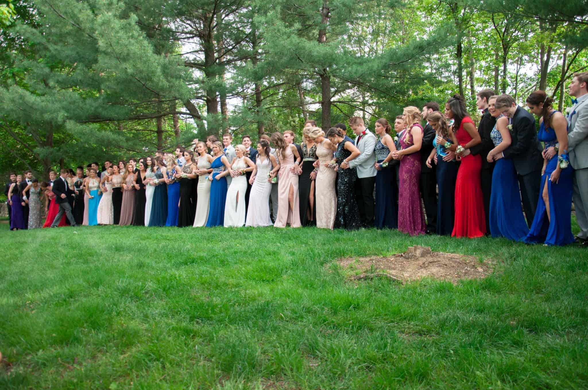 Baile de finalistas à porta? Como poupar e tornar este dia memorável grupo extenso de jovens rapazes e raparigas, vestidos de gala, posam para a fotograqfia de grupo num relvado no dia do seu baile de finalistas