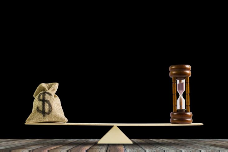 uma balança feita apenas com uma simples e pequena tábua de madeira com uma ampulheta e um saco de dinheiro nas extremidades, simbolizando o potencial de investir