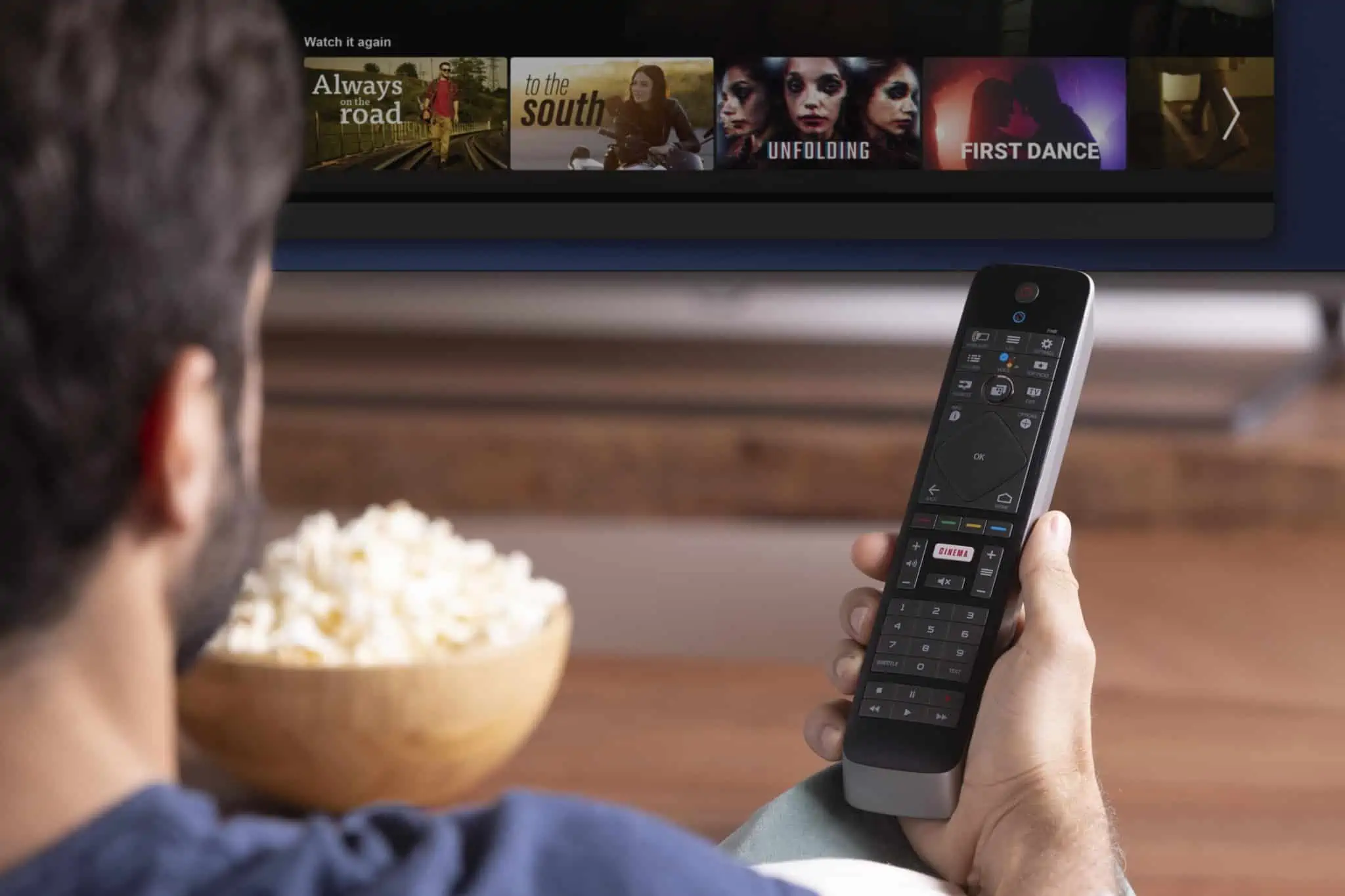 Como poupar nas subscrições de serviços e aliviar as despesas mensais jovem rapaz a ver TV com subscrições, a segurar comando e uma taça de pipocas