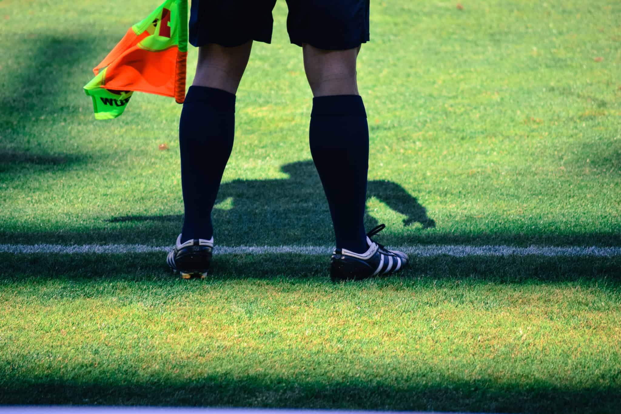 Bolsa de formação desportiva. Como devo gerir a carga fiscal? imagem de árbitro, apoiado por uma Bolsa de formação desportiva, junto á linha que delimita o campo de futebol, seguando uma bandeirola colorida