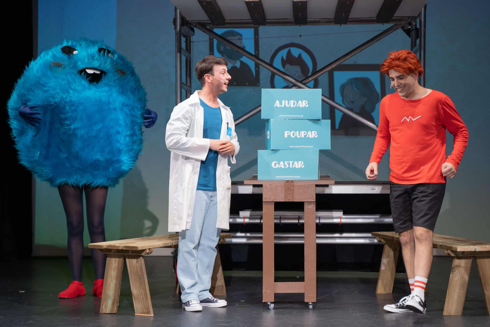 Uma cena da peça de teatro Doutor Finanças e a bata mágica, onde se vê o Bichinho da Poupança e os dois irmãos: Miguel e João.