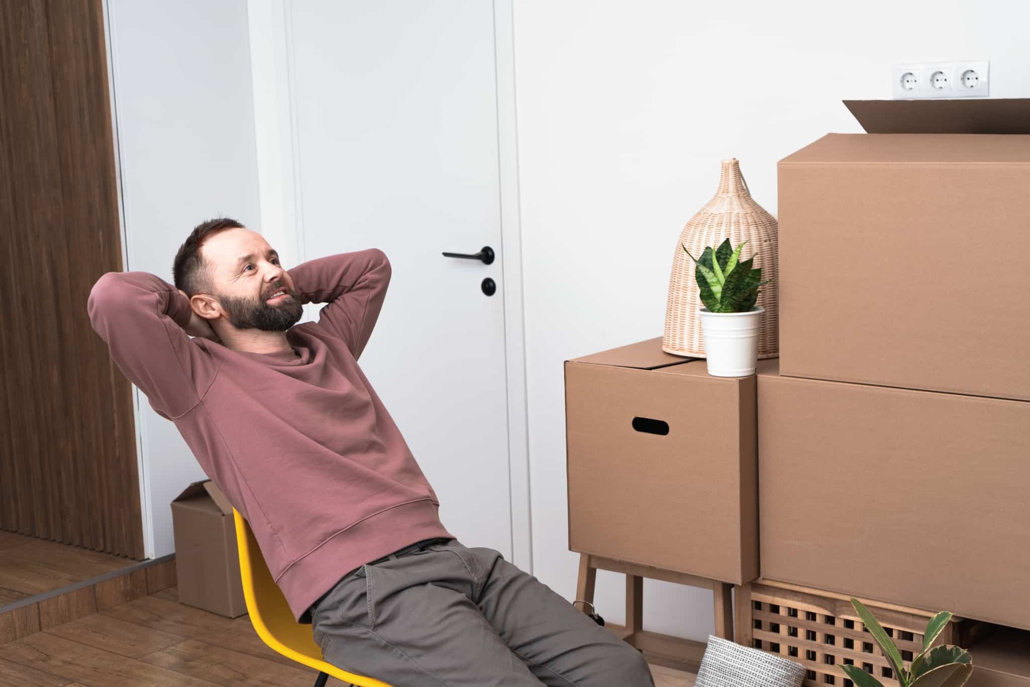 Prepare a compra da sua casa: 5 pontos que não pode “saltar” jovem rapaz, sentado numa cadeira amarela, por entre uma série de caixas de mudanças, a celebrar a compra de casa concretizada depois de alguns passos importantes