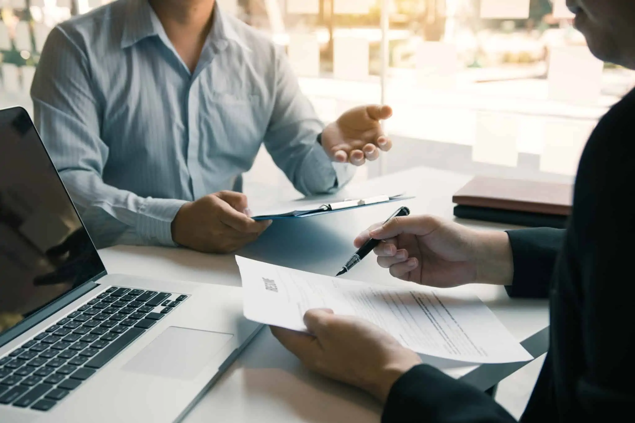 10 diferenças entre trabalhar para o Estado ou para o privado Mãos de homem seguram contrato de trabalho Portugal e homem à frente aponta para a folha com pasta na mão