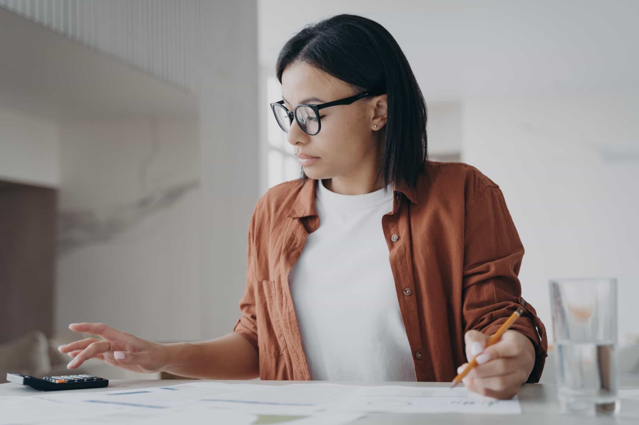 jovem mulher, a trabalhar, analisa documentos e faz contas para cumprir as suas obrigações enquanto trabalhadora por conta de outrem e também a recibos verdes