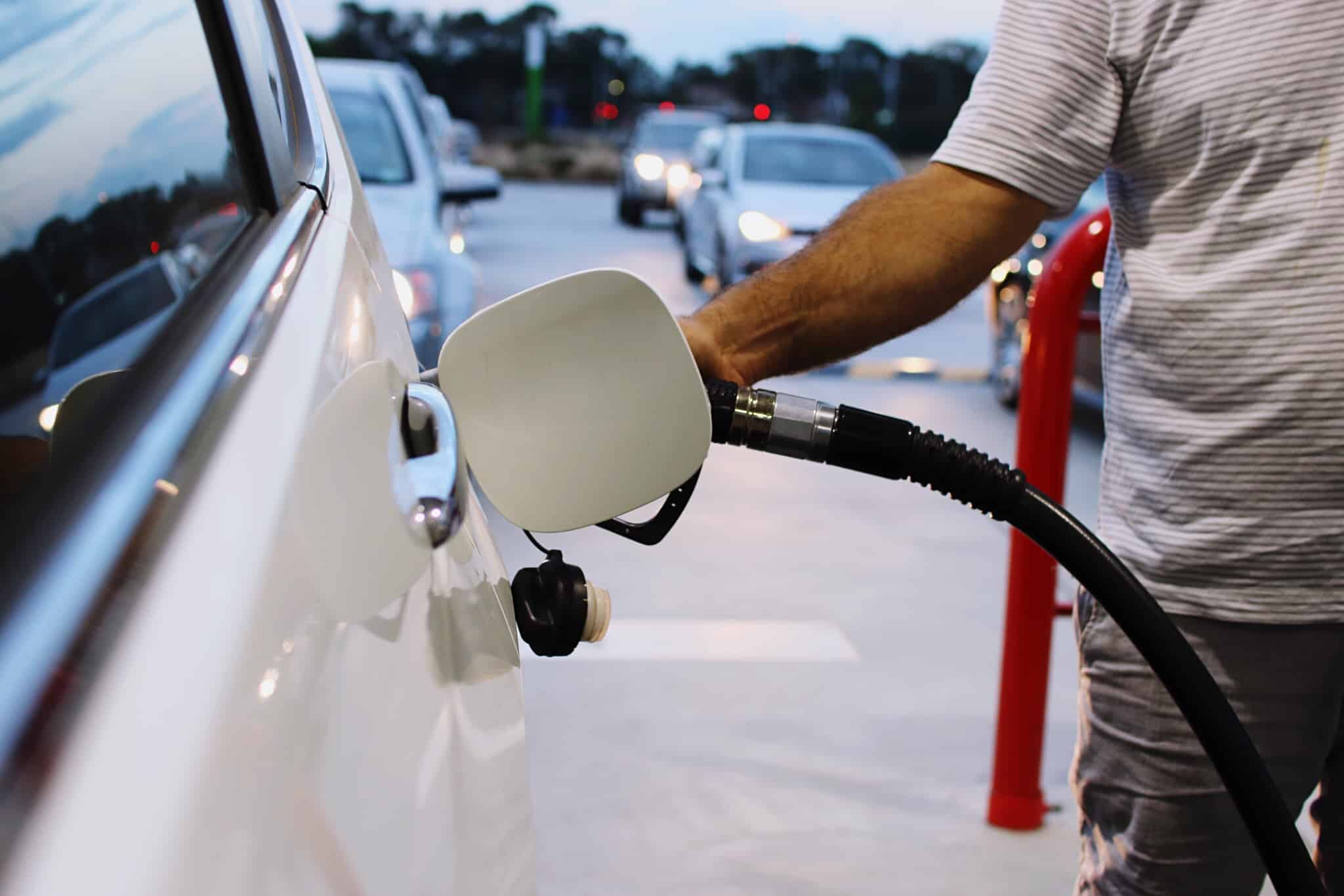 homem bastece combustível num automóvel branco em posto de abastecimento