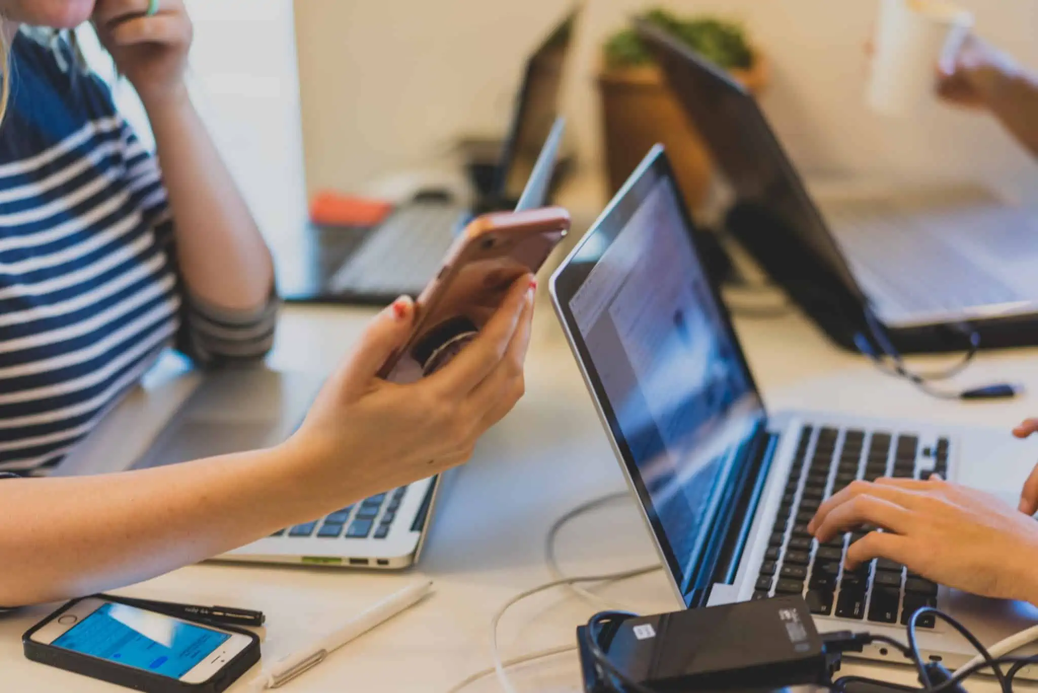Mesa com alunos do Ensino Superior ao computador e rapariga a segurar em telemóvel