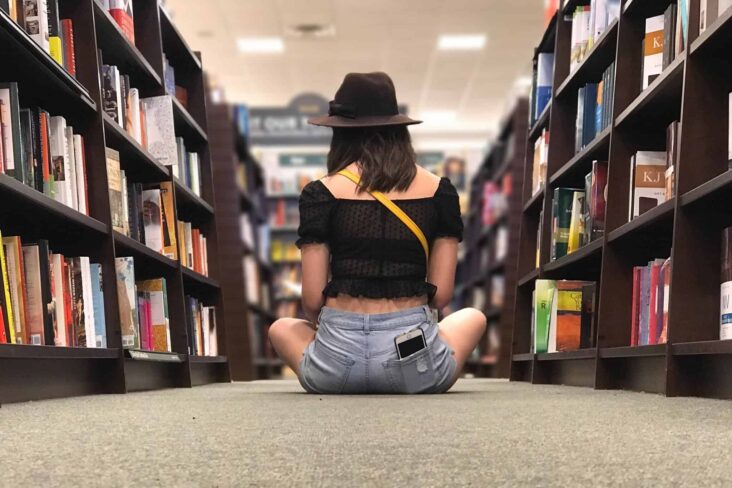 jovem mulher sentada no chão de um corredora de uma biblioteca prepara a entrada na universidade