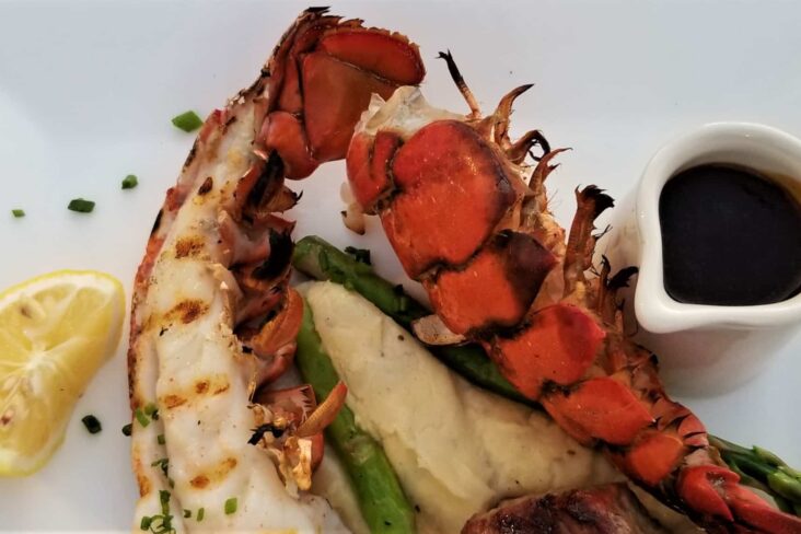 Carabineiro grelhado, servido com um molho sobre uma cama de legumes