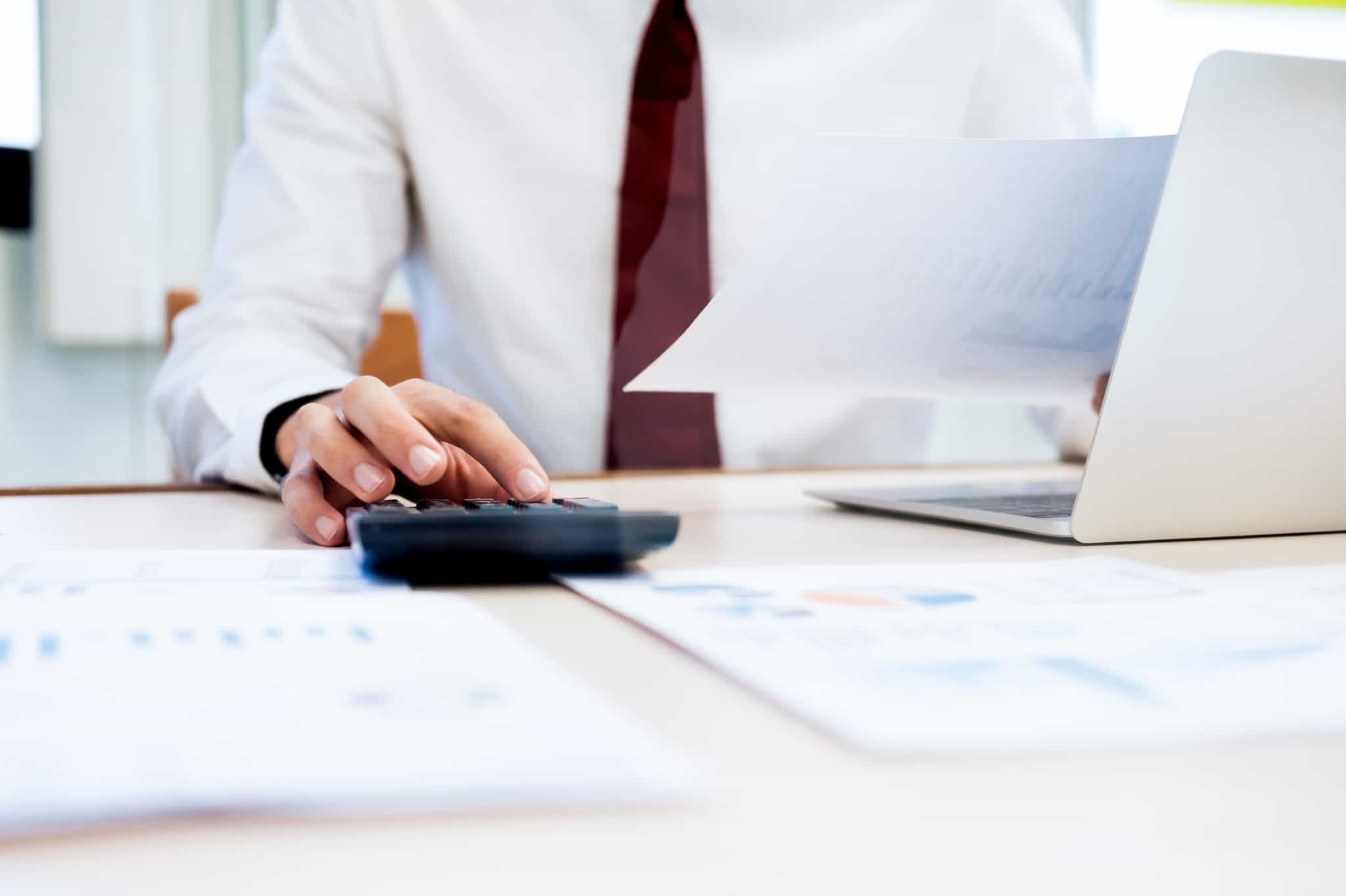 homem faz contas, vestido formalmente de gravata, faz contas num calculadora e analisa as contas que deram erro e podem dar origem a reclamação graciosa