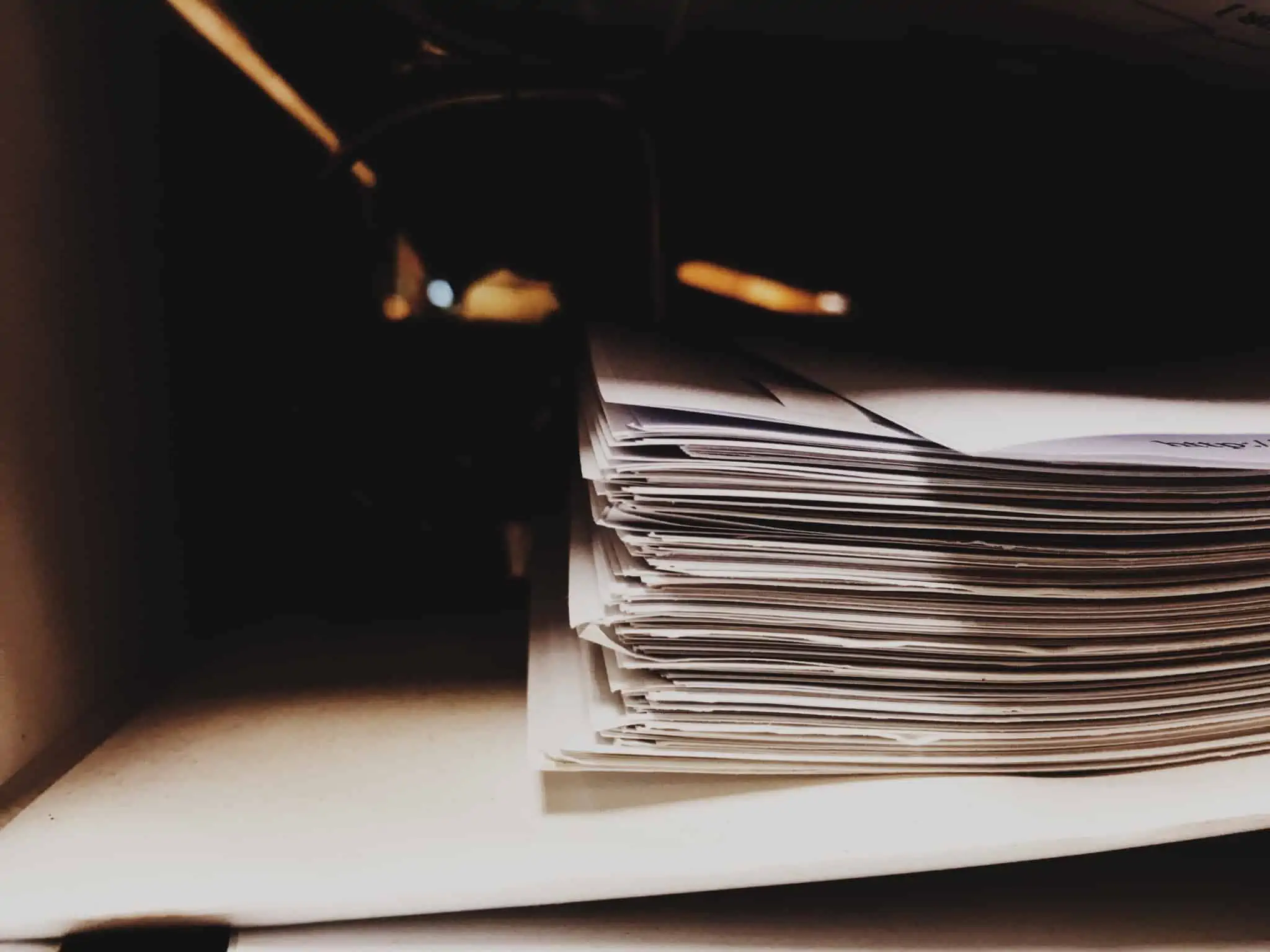 Reclamação de um serviço público essencial: O que é e como funciona? pilha de papeis, documentos com reclamação serviço público essencial, em cima de uma mesa mesa, apenas em fundo escuro e desfocado