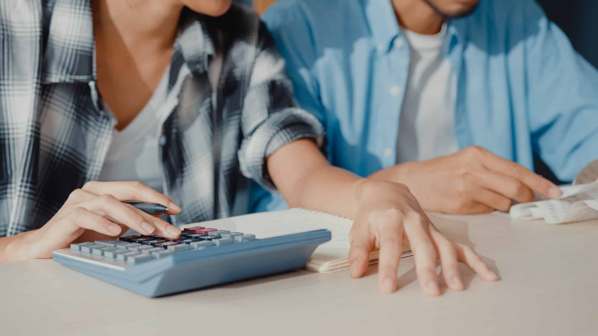 Crise financeira? 6 dicas para se preparar da melhor forma jovem casal confere faturas e documentos usando a máquina de calcular preparanod-se para ajustra o orçamento em tempos de crise financeira