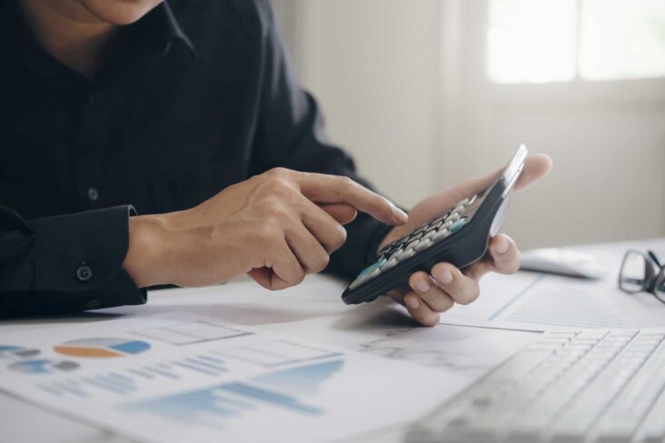 Homem a fazer contas numa calculadora, em cima de uma pilha de papéis