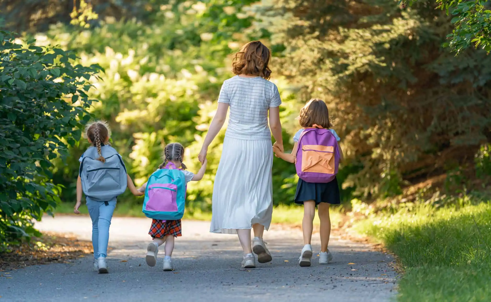 O seu filho vai entrar no primeiro ciclo? O que deve preparar Mãe a caminhar com três filhas de costas com mochilas simbolizando primeiro ciclo