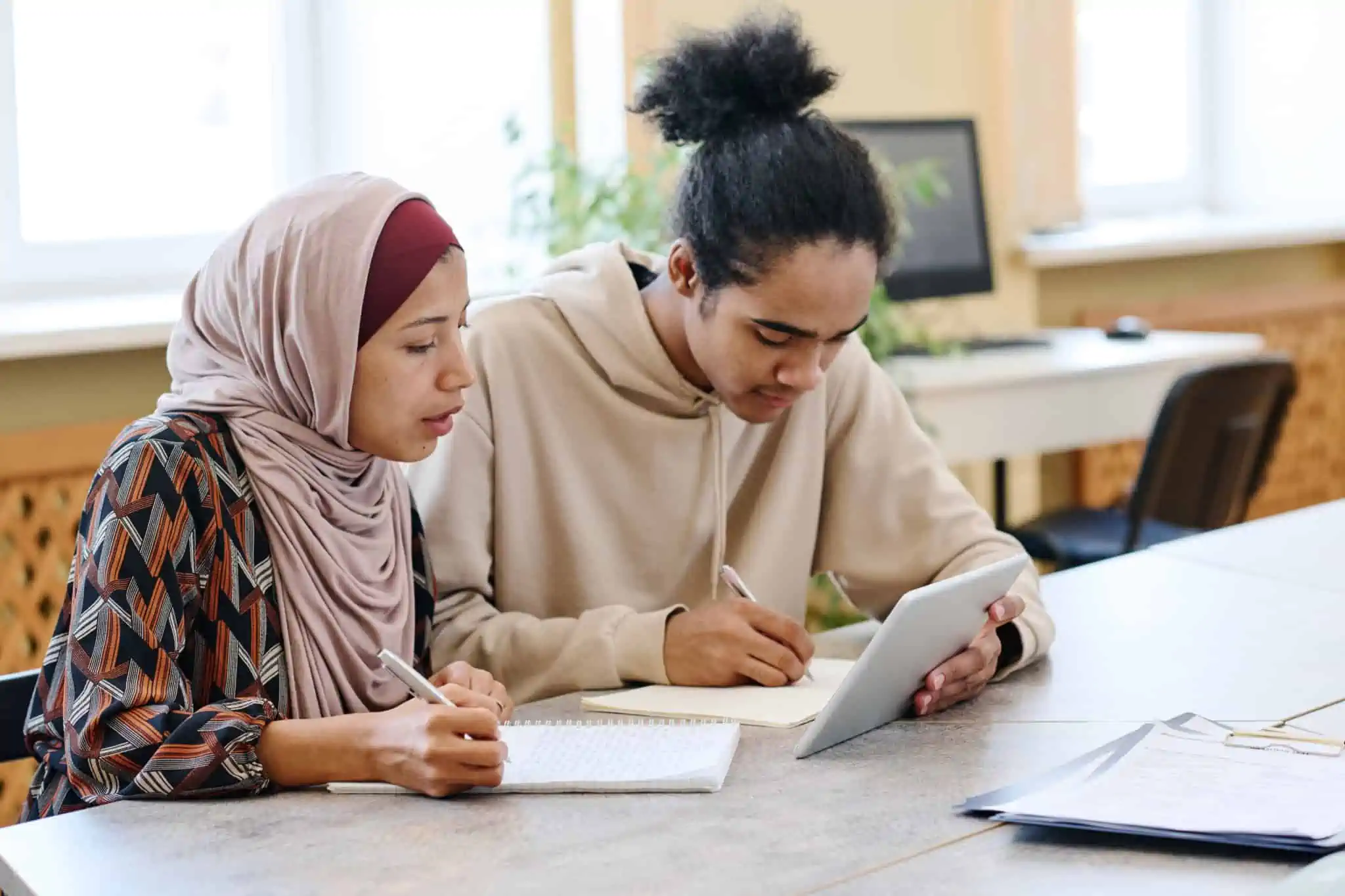 Dois imigrantes sentados a uma mesa com papéis e ipad a estudar