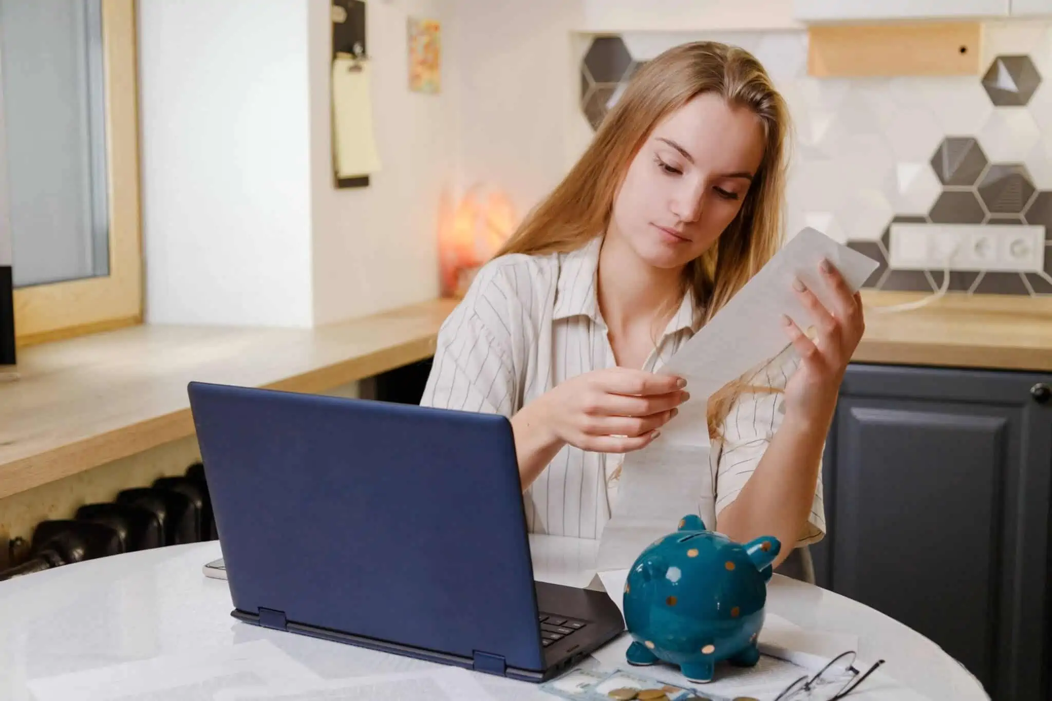 jovem mulher, a beneficiar do complemento por dependência, analisa com um ar preocupado um longo recibo, de entre alguns domcumentos que estão em cima da mesa , junto ao computador e ao porquinho mealheiro