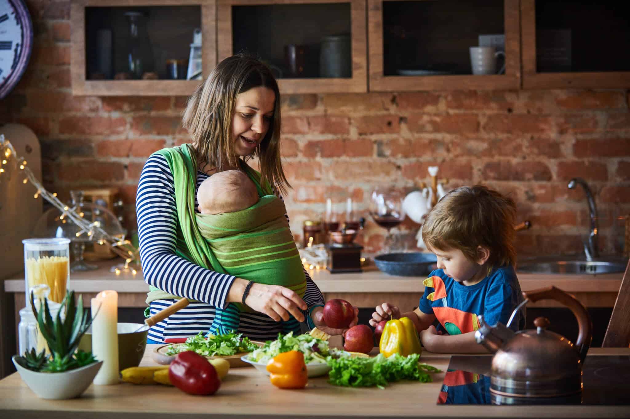 jovem mãe com um bebe ao colo e um pequeno sentado junto a si, na cozinha, a prepararem uma refeição, fazendo assim face às despesas que acrescem com filhos e que obrigam a ajustar o orçamento