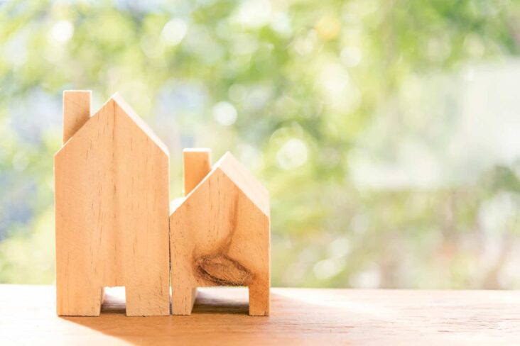 Duas casas de madeira em cima de mesa com arbustos à frente para simbolizar arrendamento ou compra