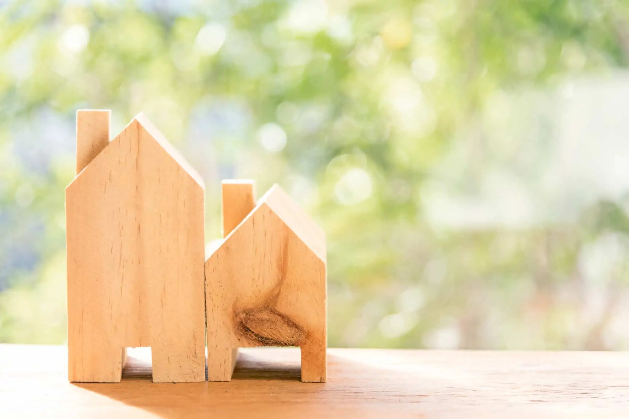 Arrendamento ou compra de casa: Como pode evoluir a prestação? Duas casas de madeira em cima de mesa com arbustos à frente para simbolizar arrendamento ou compra