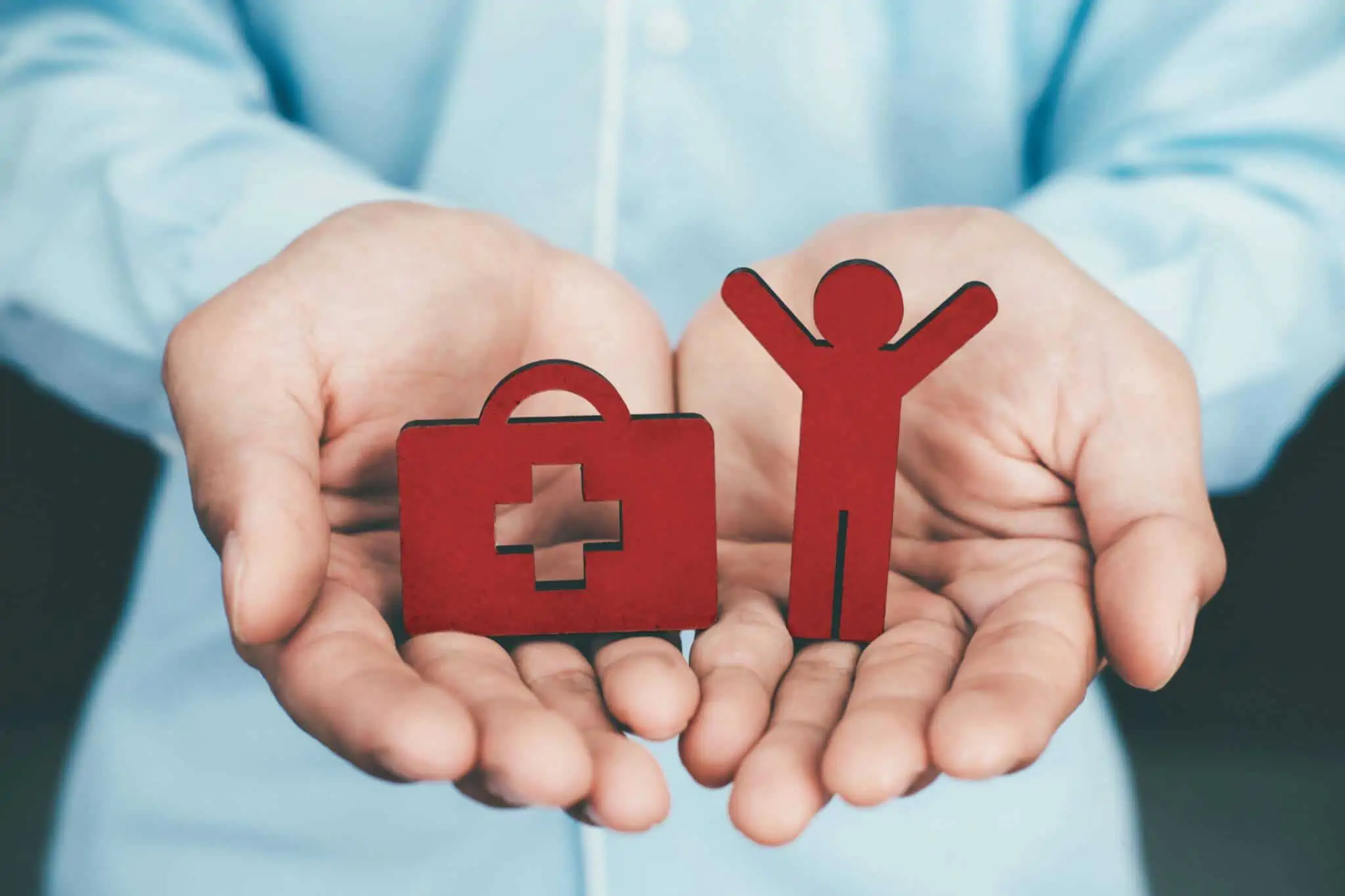 Seguro de vida: Como escolher entre coberturas IAD, ITP e IDPAC? Mãos de homem a segurar peças madeira mala de emergência e boneco a simbolizar coberturas de seguro de vida