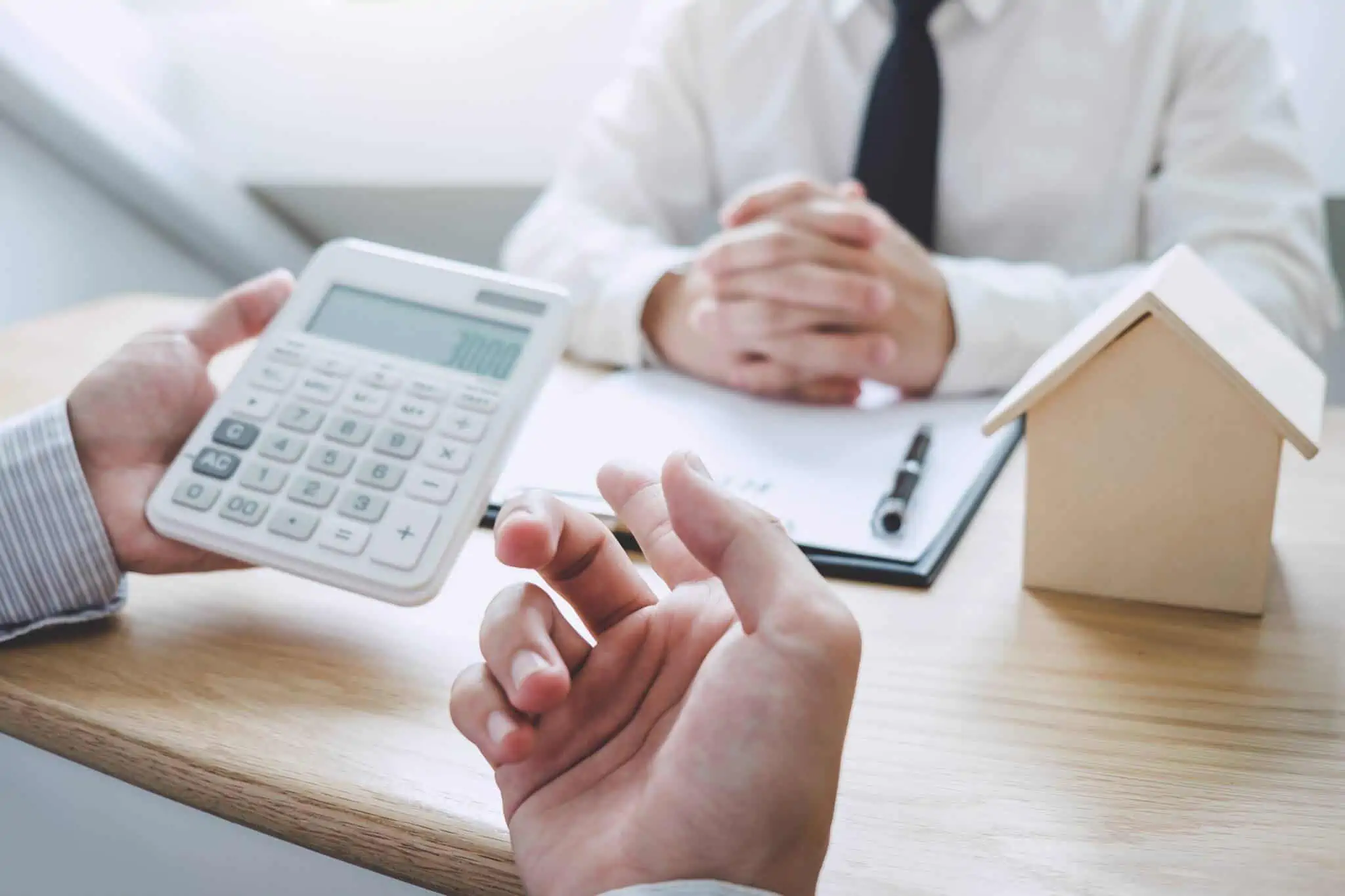Comprar casa antes de vender a minha, devo fazê-lo? mãos que usam uma calculadora , diante de um jovem homem que apresneta documentos referentes a um imóvel, decide se deve comprar casa antes de vender