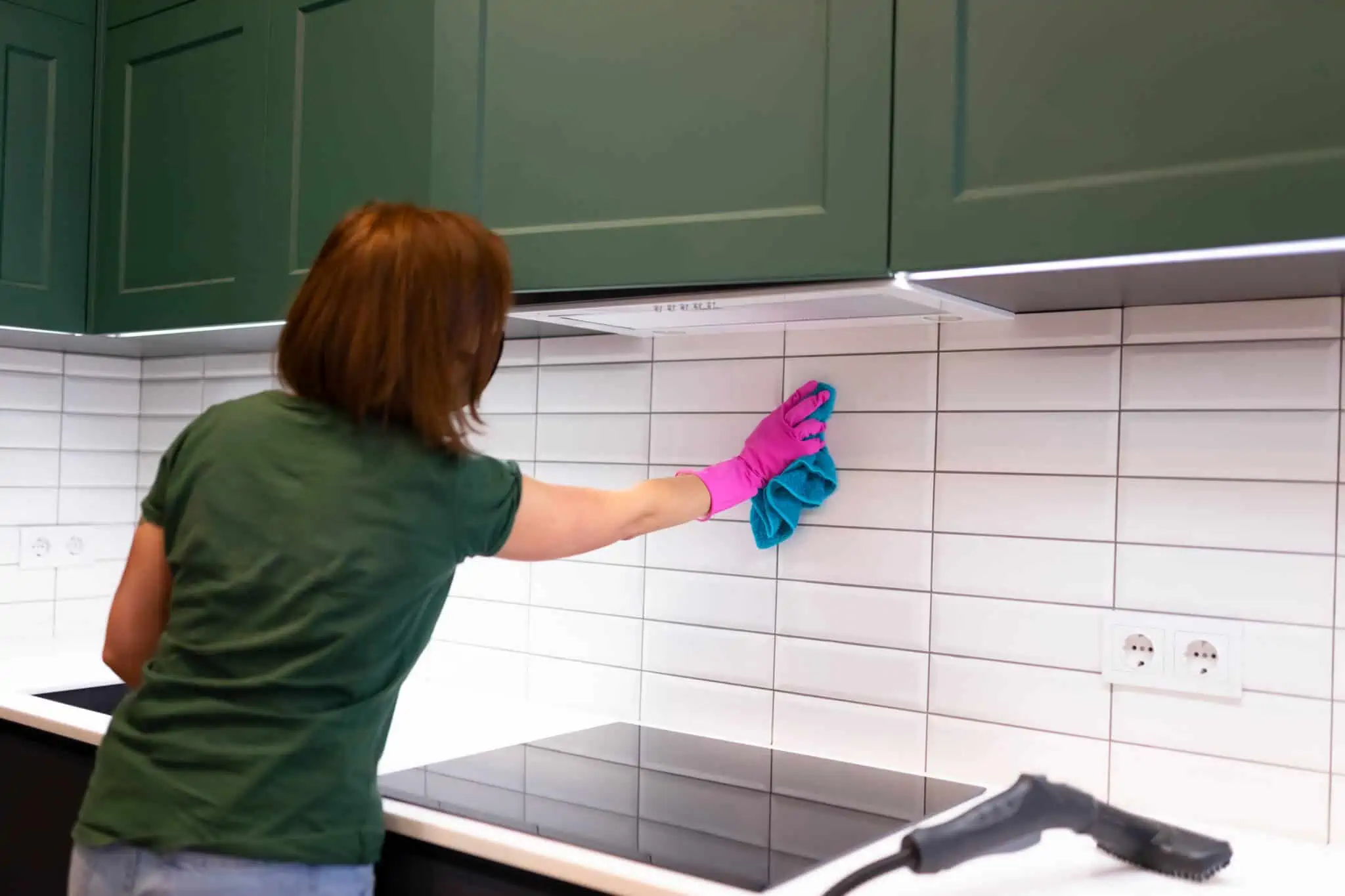Trabalho doméstico: Como declarar ao Fisco? jovem mulher, empregada doméstica, limpa os azulejos na cozinha com pano e máquina de limpeza