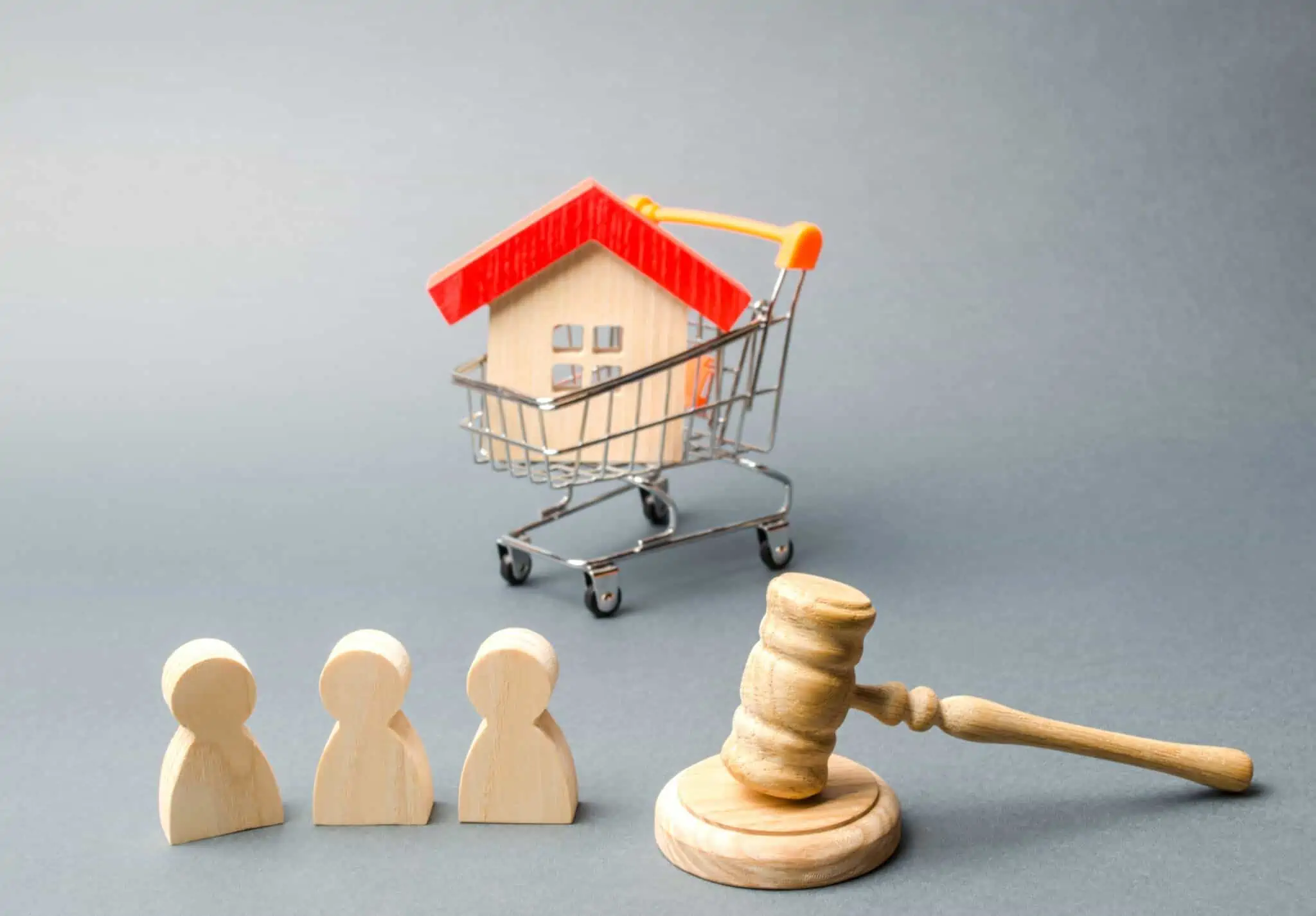 leilões das finanças referentes a casas ilustrados por um mini carrinho de compras de supermercado que leva lá dentro uma casa, em madeira, rodeado por peões de madeira e um martelo, tudo em madeira também
