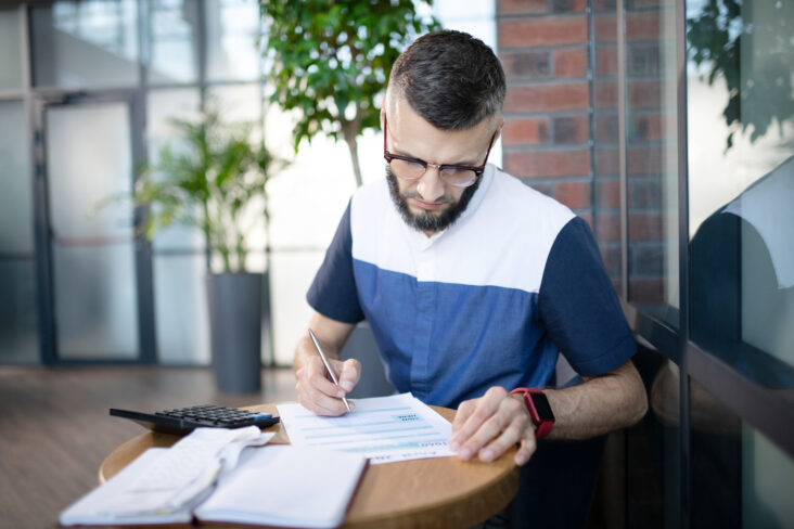 jovem empresário, à mesa do seu escritório, consulta documentos para garantir o cumprimento fiscal