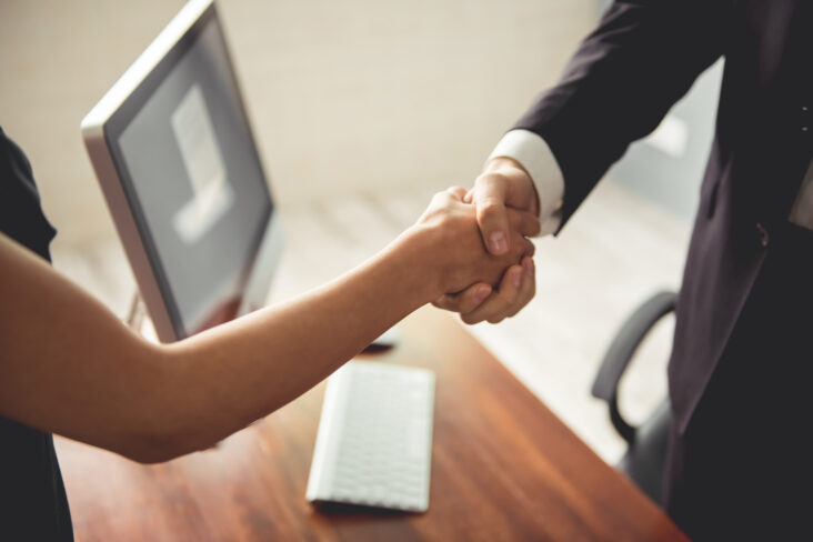 homem e mulher trocam um aperto de mão aquando da entrevista para emprego, exemplificando o que as empresas estão à procura no recrutamento