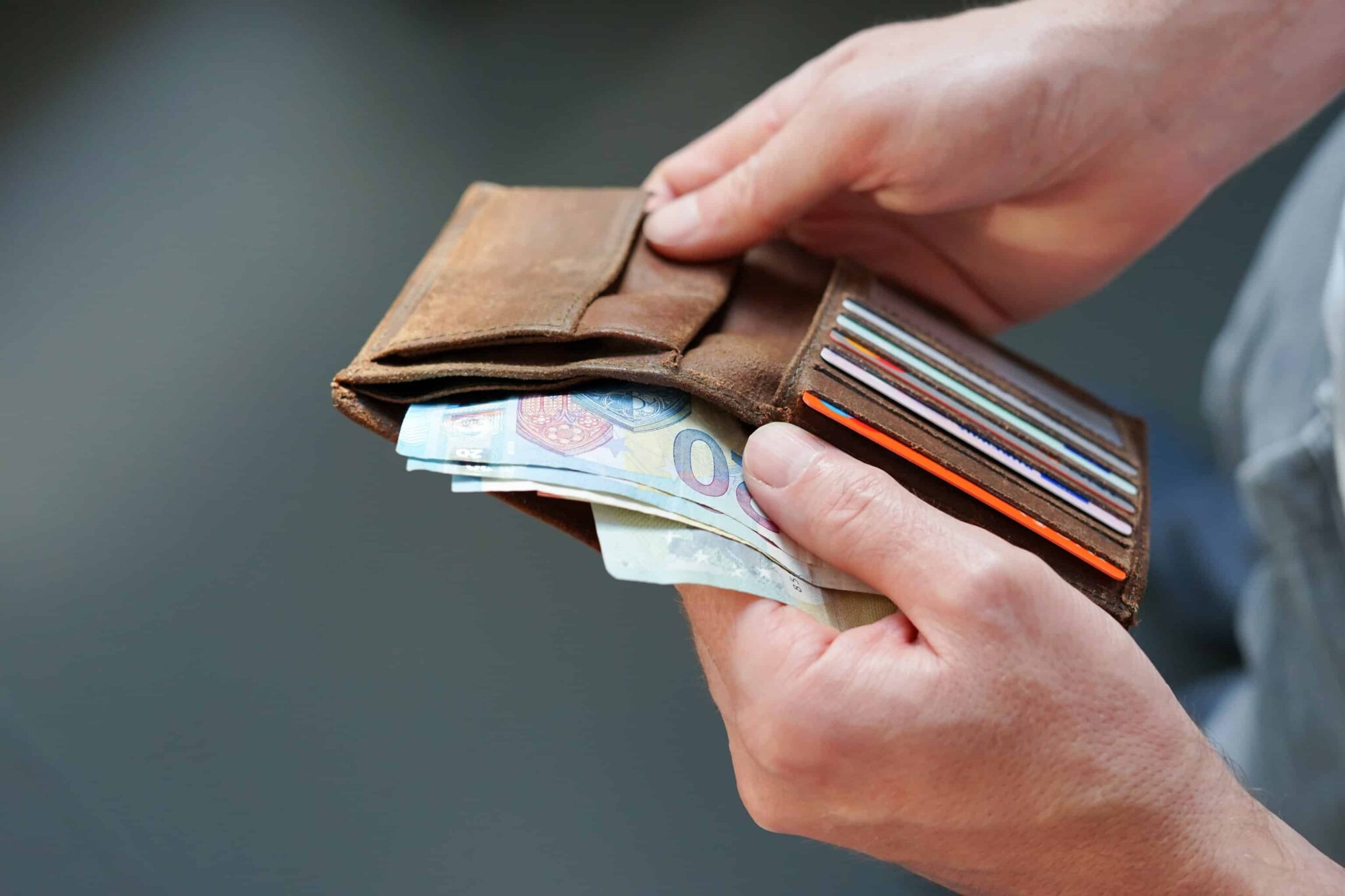 12 dicas para controlar gastos e poupar dinheiro home abre carteira de bolso e conta as notas de euro que tem, ilustrando a importancia de reduzir gastos para poupar dinheiro mensalmente