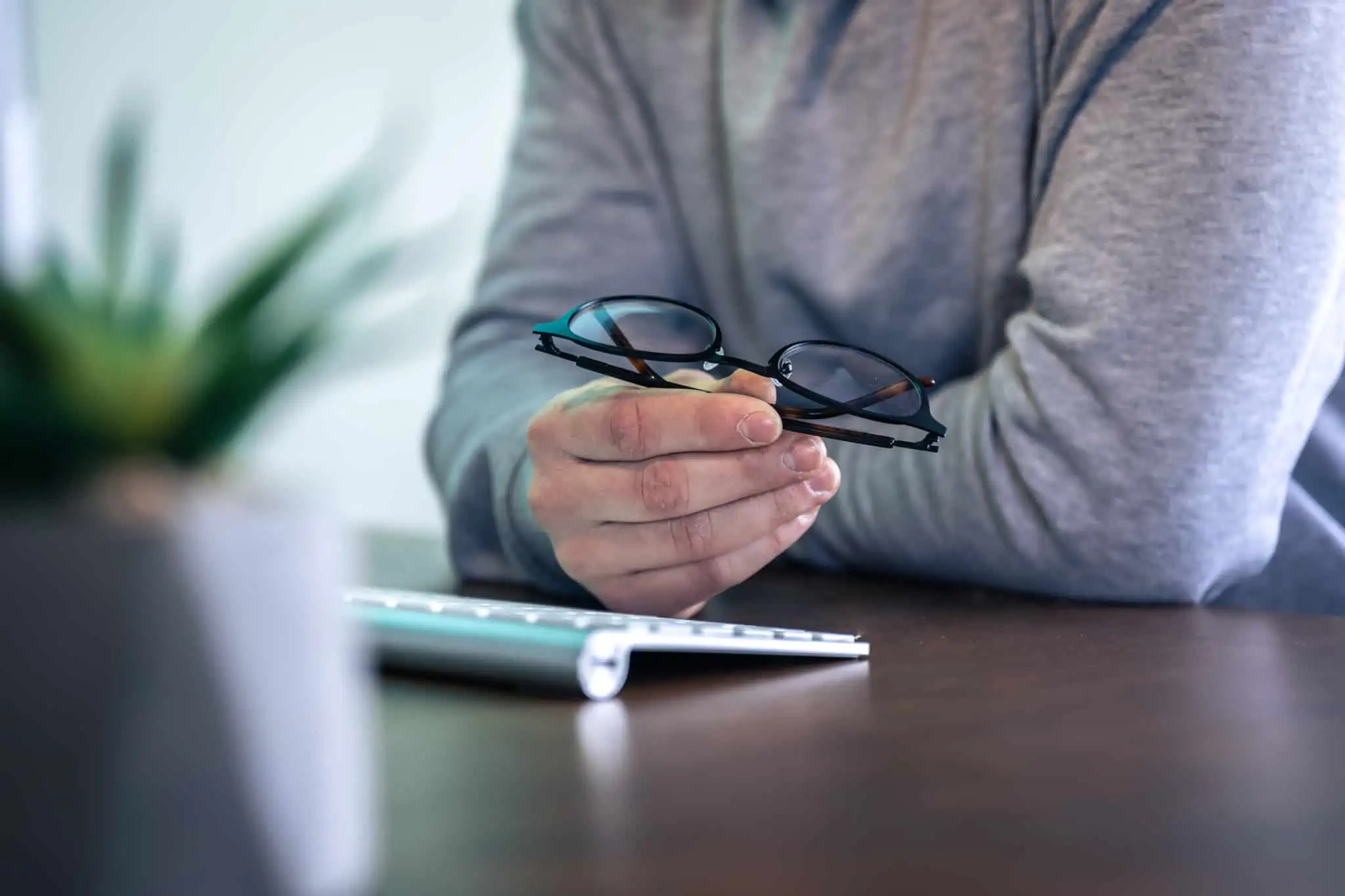 Usa óculos ou lentes no trabalho? Empresas podem ter de pagar homem, sentado frente ao ecran, repousa mão sob o teclado do computador segurando os óculos, sendo qte também usa lentes de contacto