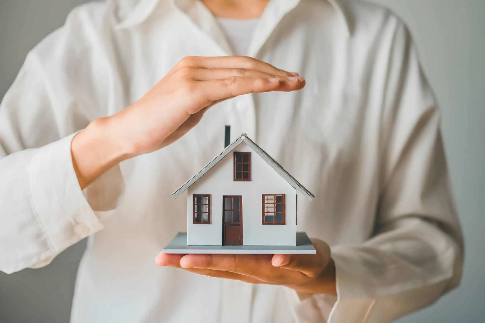 Posso anular os seguros da casa? Pessoa a segurar maquete de casa numa mão e a proteger casa com a outra para simbolizar seguros