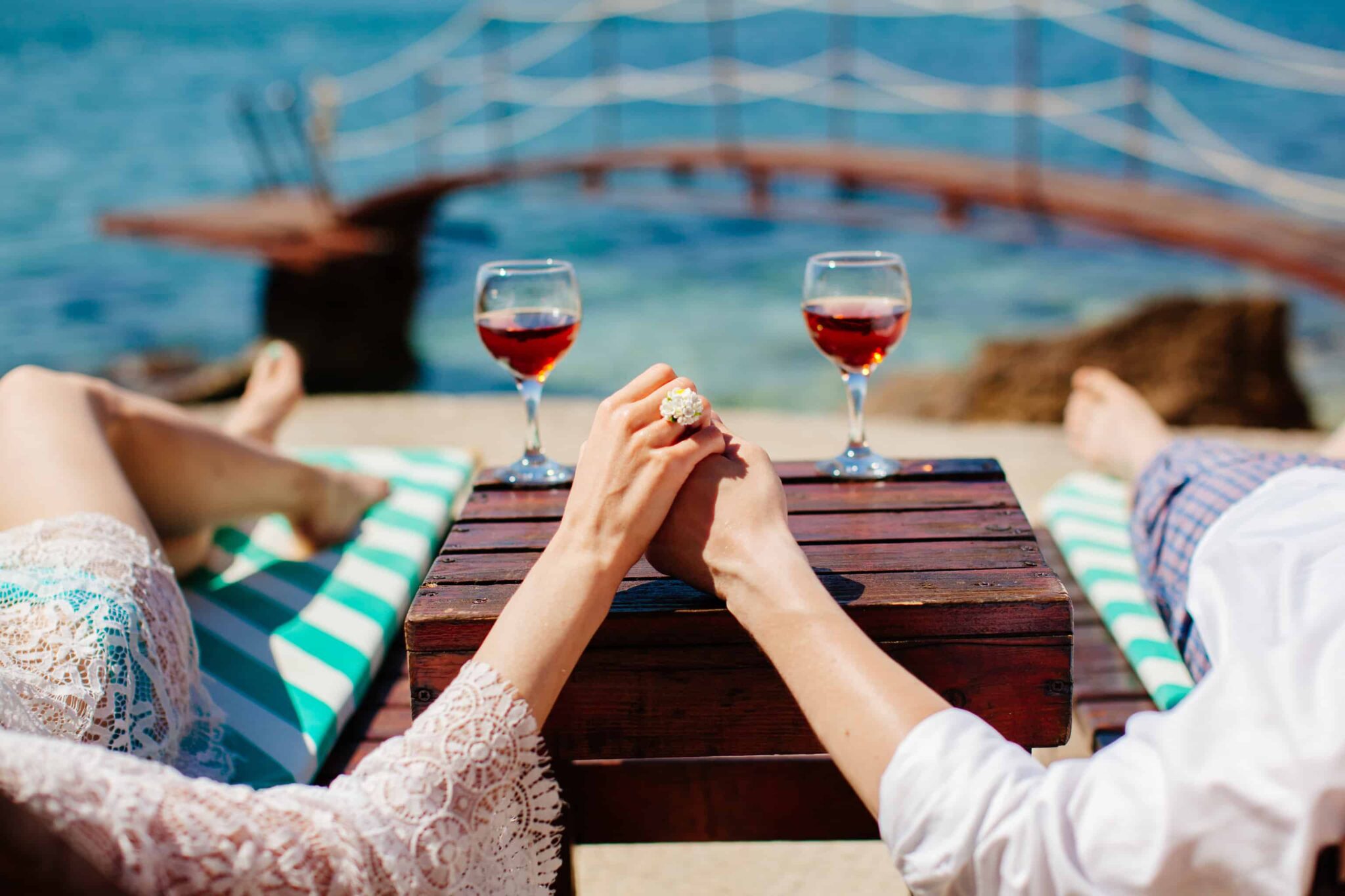 jovem casal de mãos dadas, deitados a relaxar junto ao mar, a aproveitar a sua lua de mel