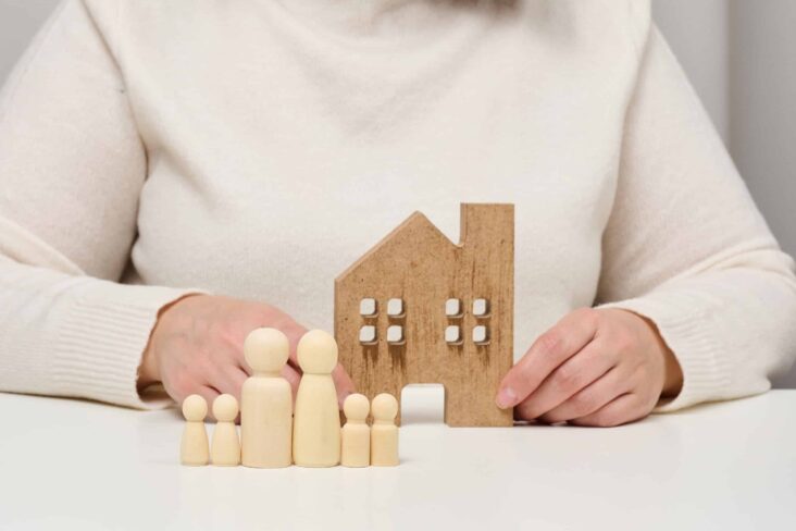 pessoa a segurar uma casa de madeira com bonecos de madeira a frente a ilustrar os seguros da casa no crédito habitação