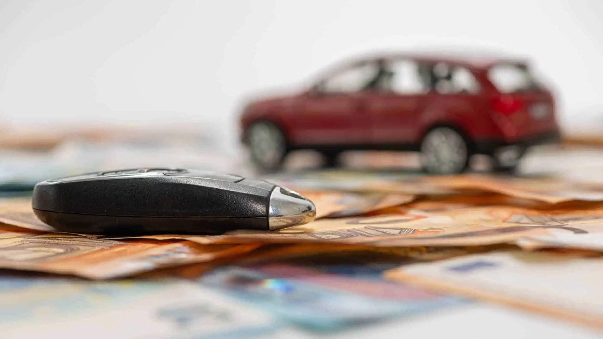 Vendeu um carro e a propriedade não foi transferida? Saiba o que fazer muitas notas de euro dispersas com uma chave de automovel em cima e em fundo desfocado um carro, rementendo para as questões da proriedade