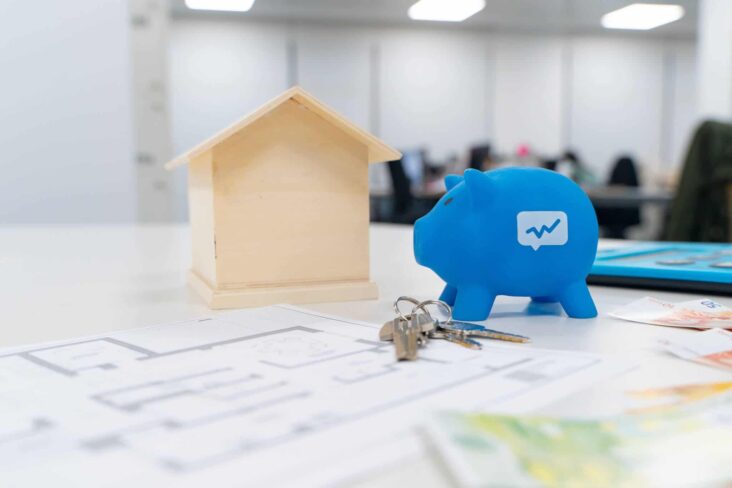 Porquinho mealheiro azul, com o logotipo do Doutor Finanças ao lado de uma casa de maneira em miniatura