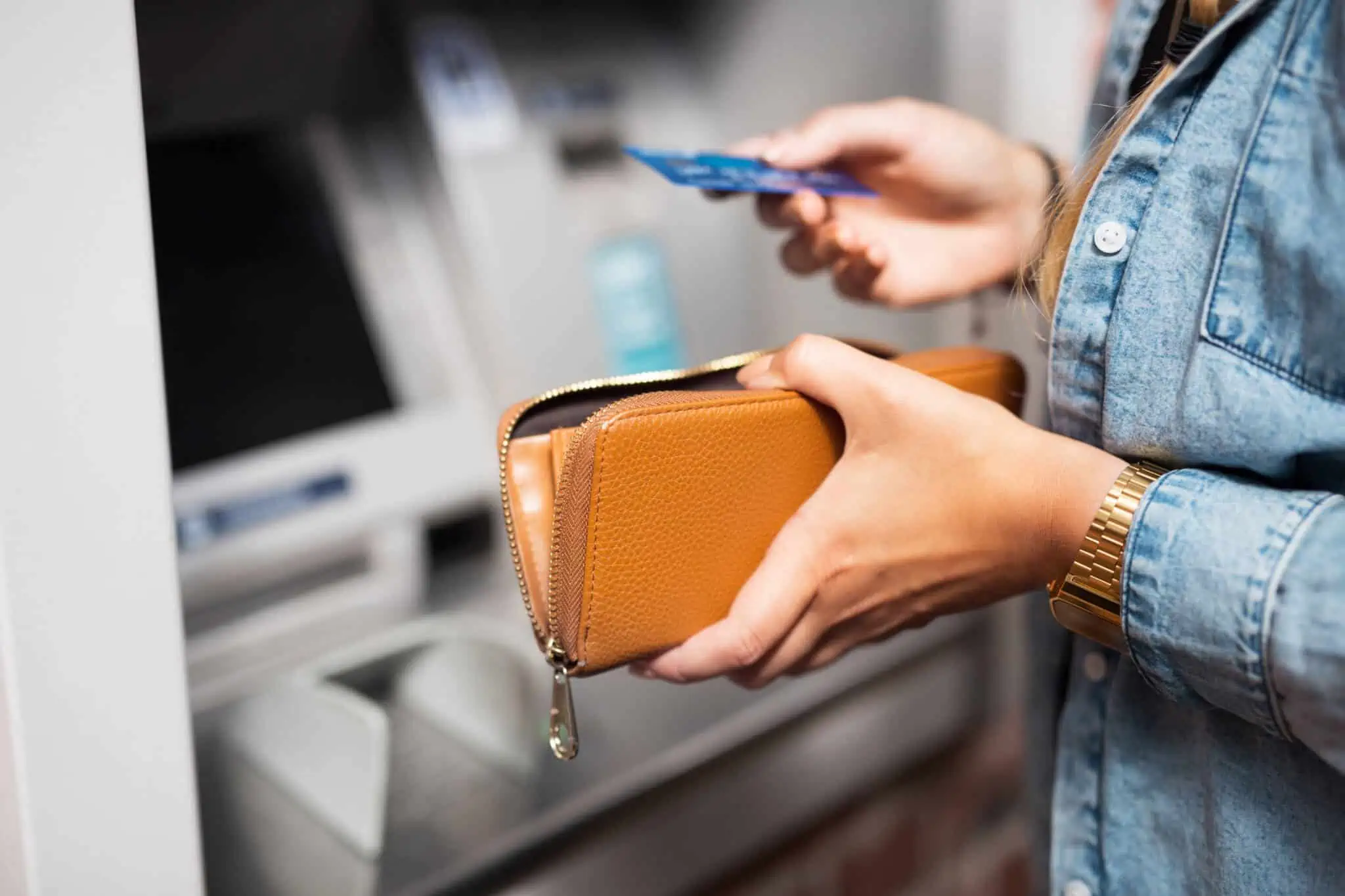 jovem mulher junto a um ATM segura cartão retirado da carteira aberta para introduzir e fazer uma transferência pelo multibanco