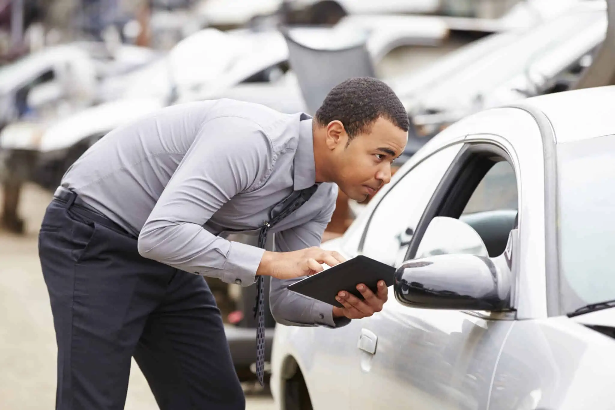 Inspeção automóvel: O que acontece em caso de reprovação? jovem homem faz a inspeção automóvel, tendo nas mãos um documento onde está a apontar todos os pontos, enquanto espreita por dentro do carro