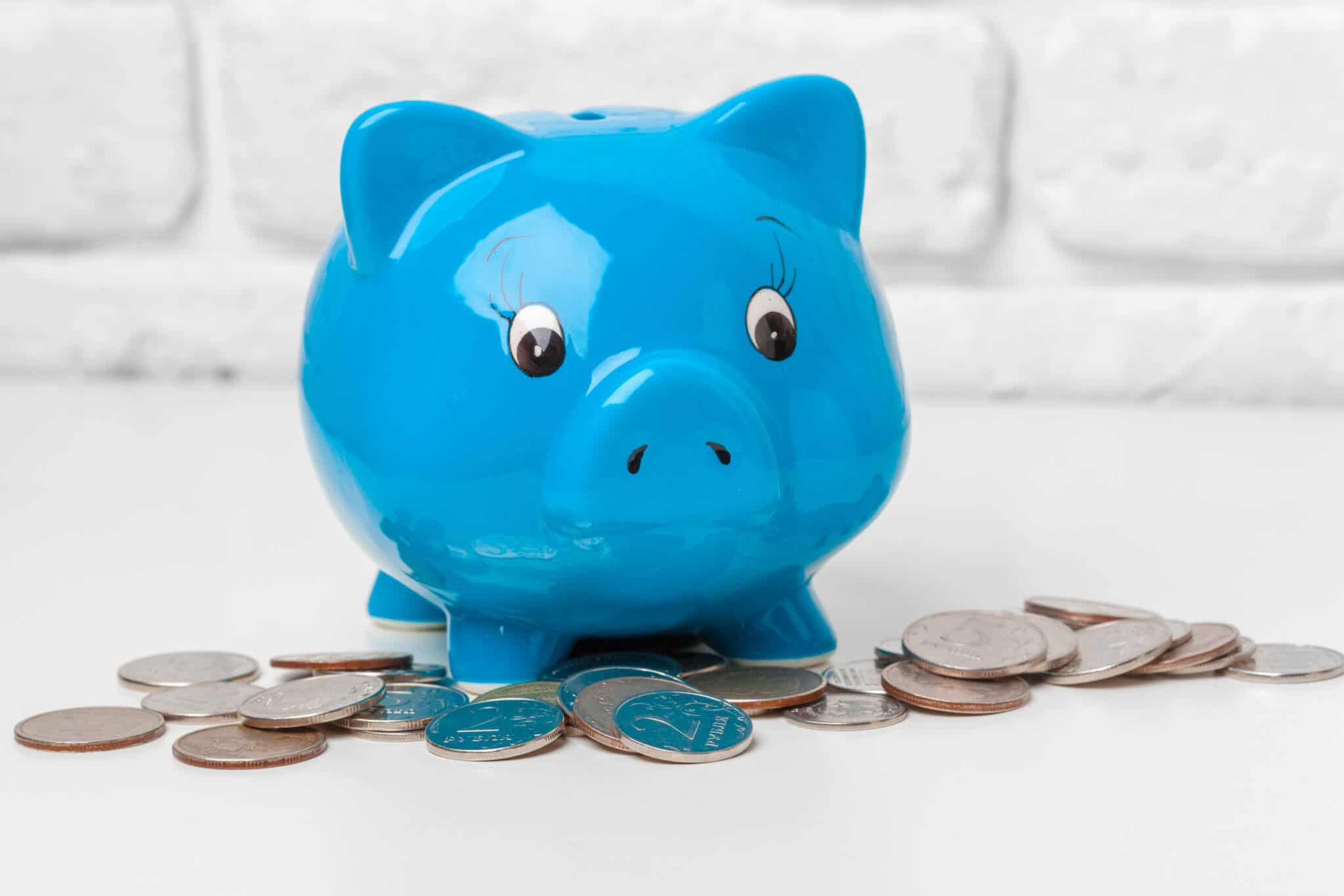 porco mealheiro em ceramica azul, em fundo branco, rodeado por pequenas moedas espalhadas fruto de uma conta poupança