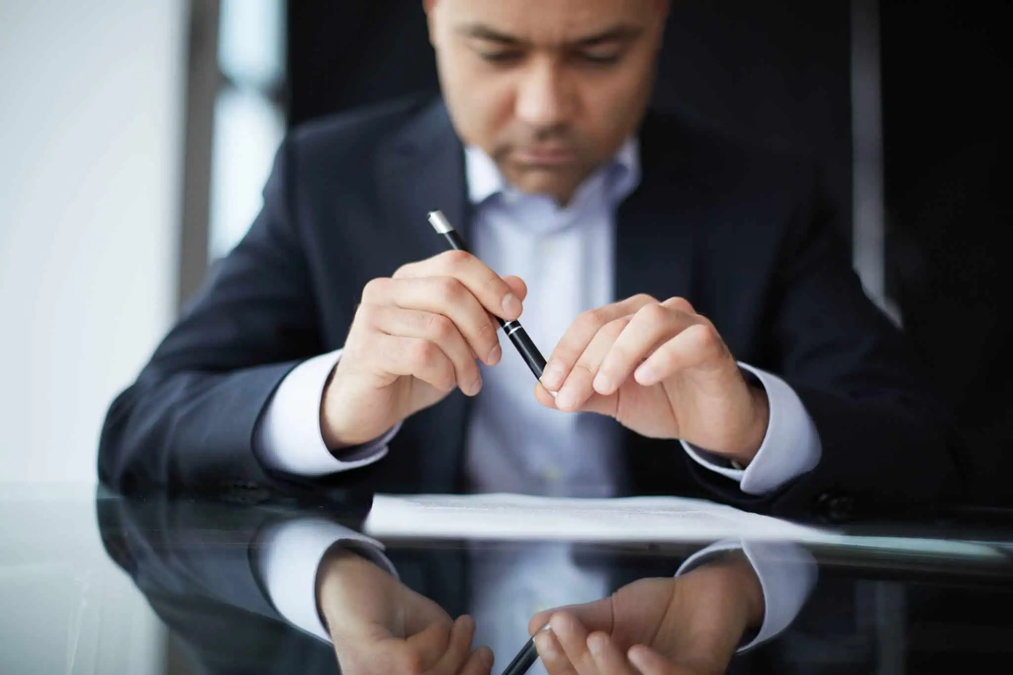 O que é um contrato de trabalho intermitente? Homem a ler um contrato, com uma caneta na mão, preparando-se para assinar o contrato