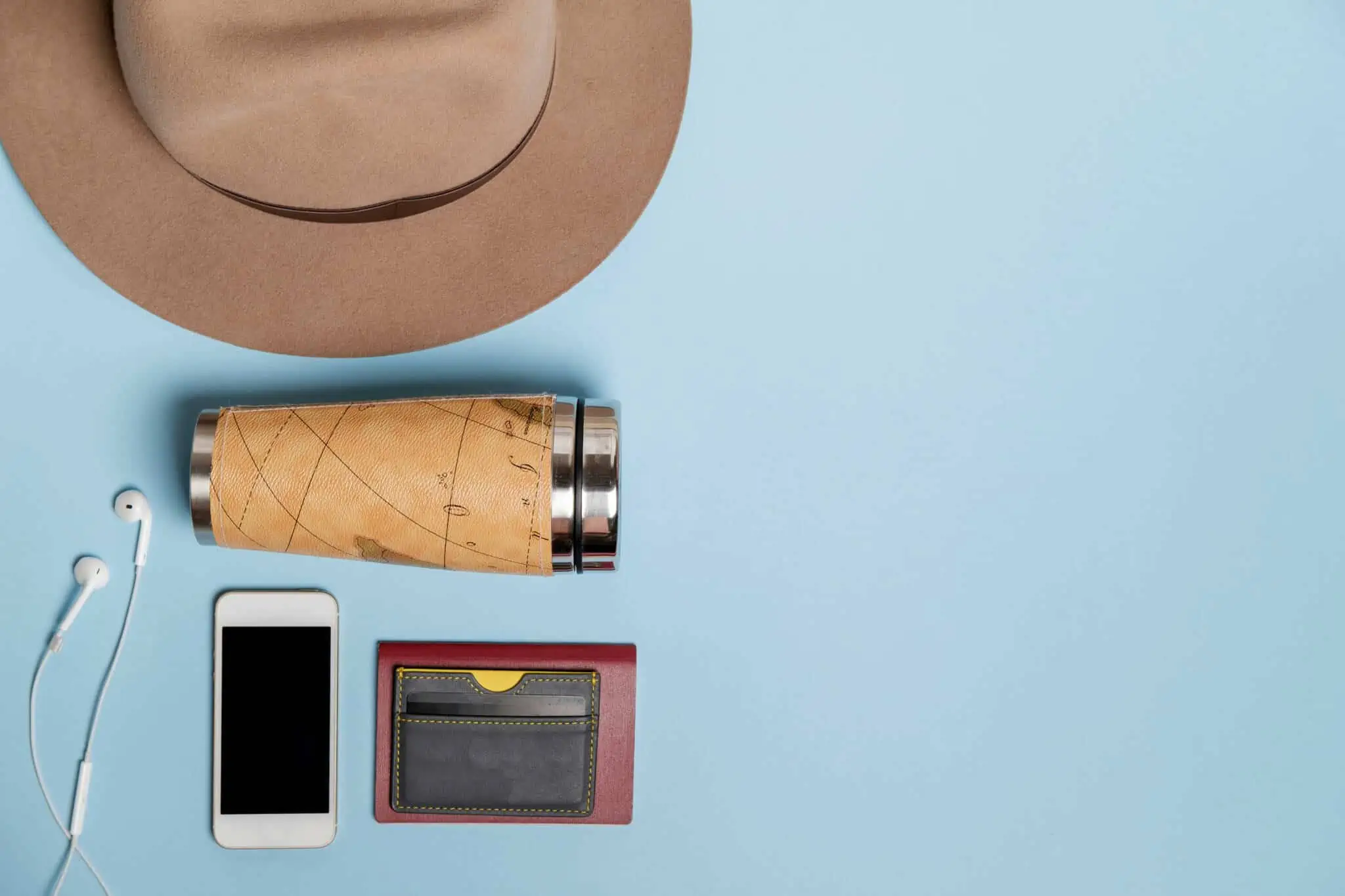 Vou viajar para o estrangeiro: Que cartões bancários devo levar? em fundo azul, alguns bojetos, como um chapéu, carteira de cartóes, um telemóvel, uma garrafa de água reutilizável, remetem para os momentos em que vamos viajar e nos quais temos de ter cartões bancários