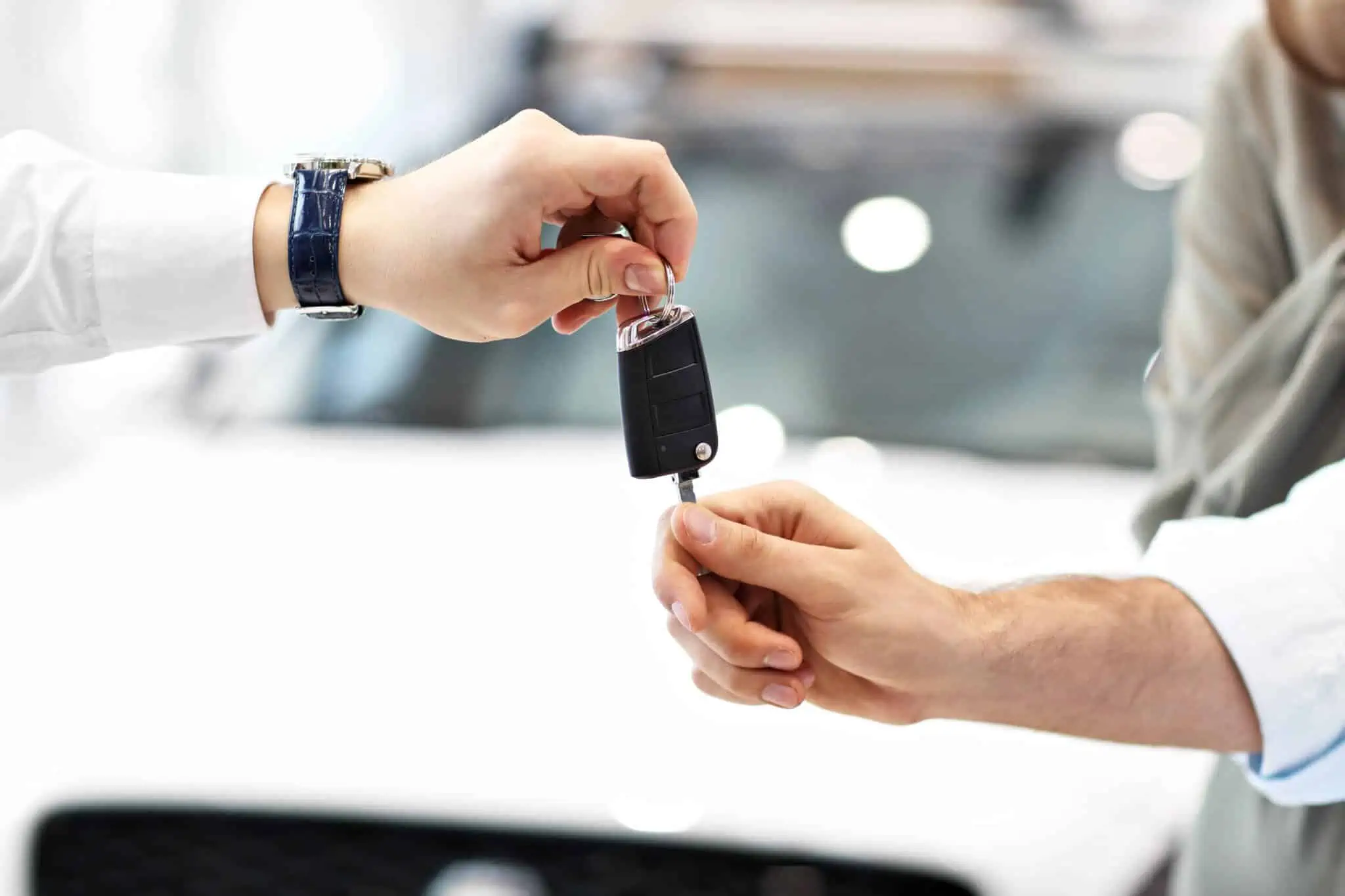 Crédito automóvel, leasing ou renting? Como escolher mãos de homem e mulher trocam chaves de carro em fundo desfiocado de um stand automóvel, no qual são praticadas s soluções crédito automóvel, leasing ou renting