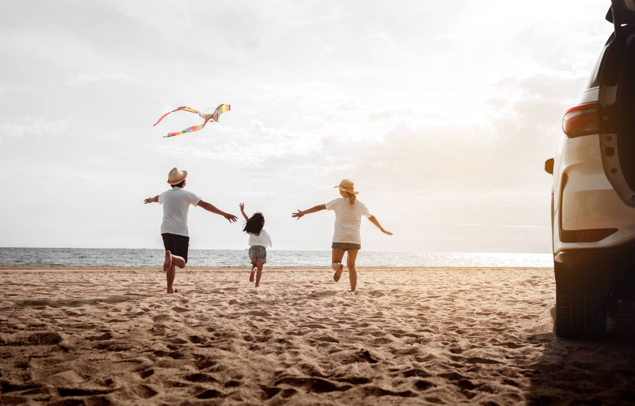 famíla corre feliz na praia, jutno do seu carro, em ambiente de quem gosta de viajar de carro nas férias