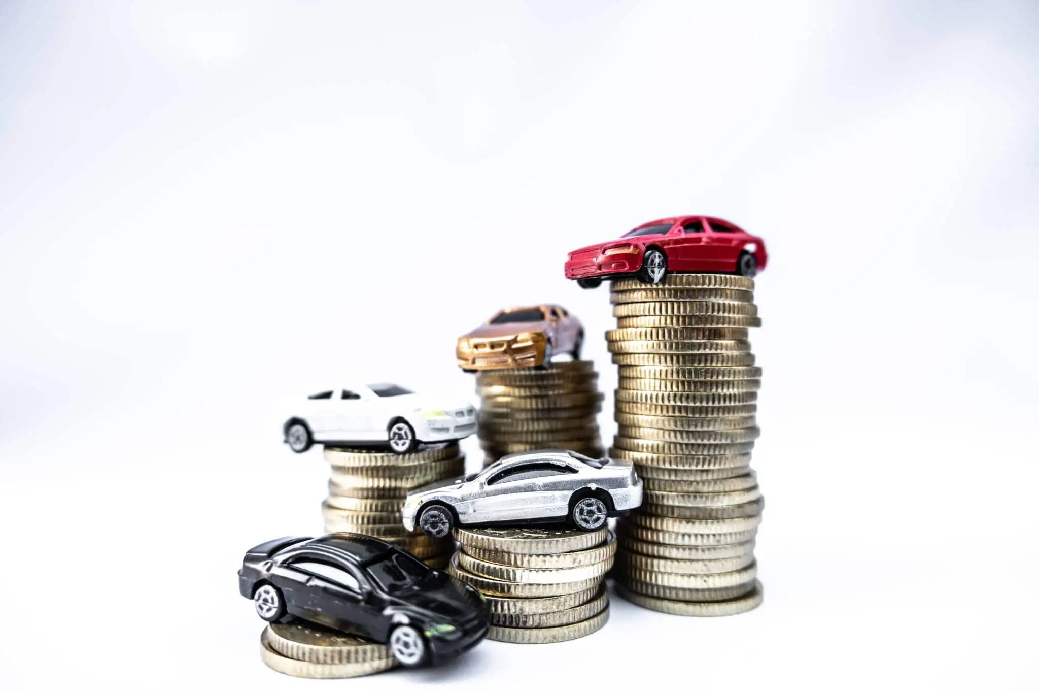 Imposto Único de Circulação: Quem tem direito a isenção? várias pilhas de moedas com diferentes carros de brincar no seu topo ilustram o pagamento do IUC