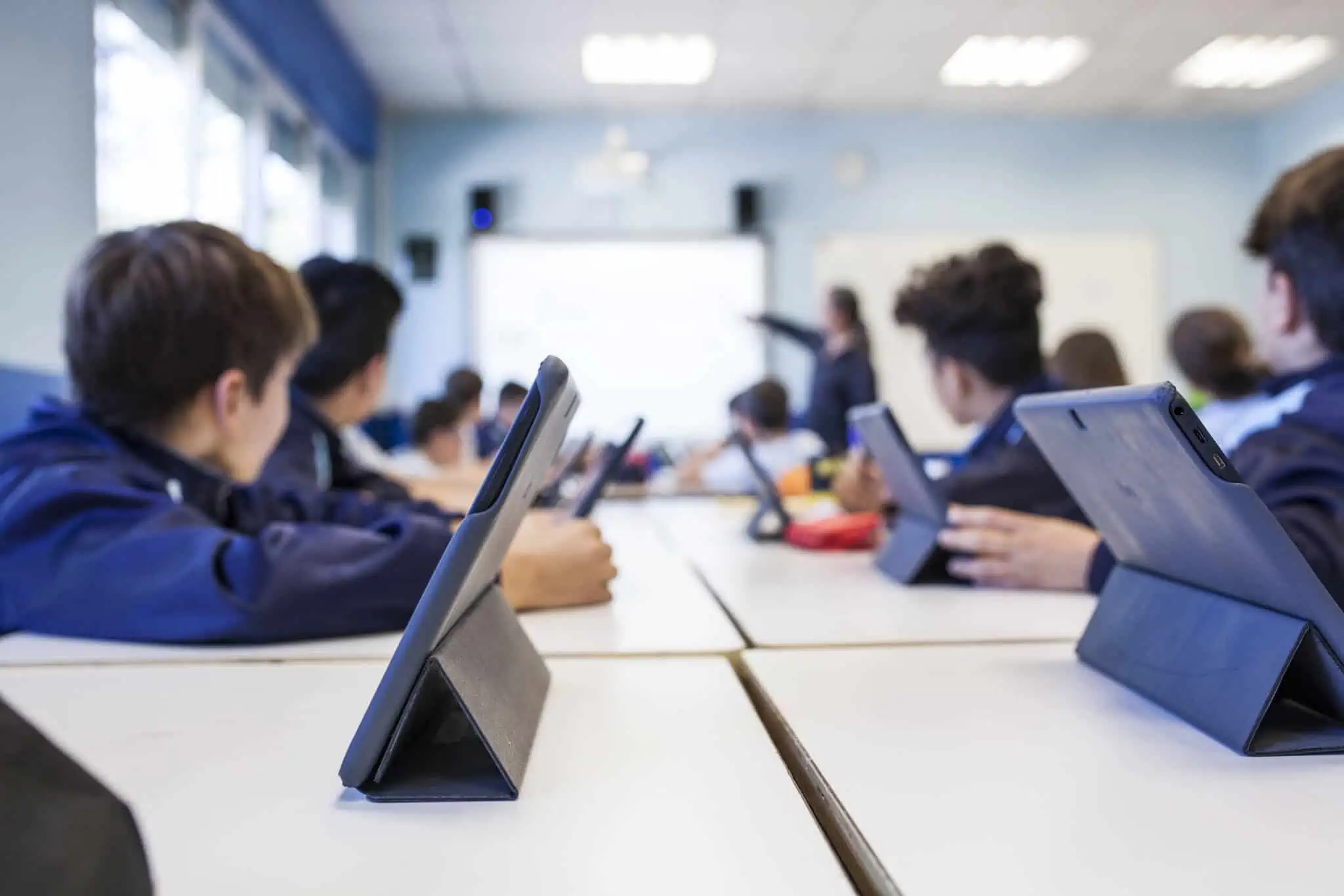 sala de estudo cheia de crianças que usam os tablets nas mesas perfiladas , os quais têm apps para estudar