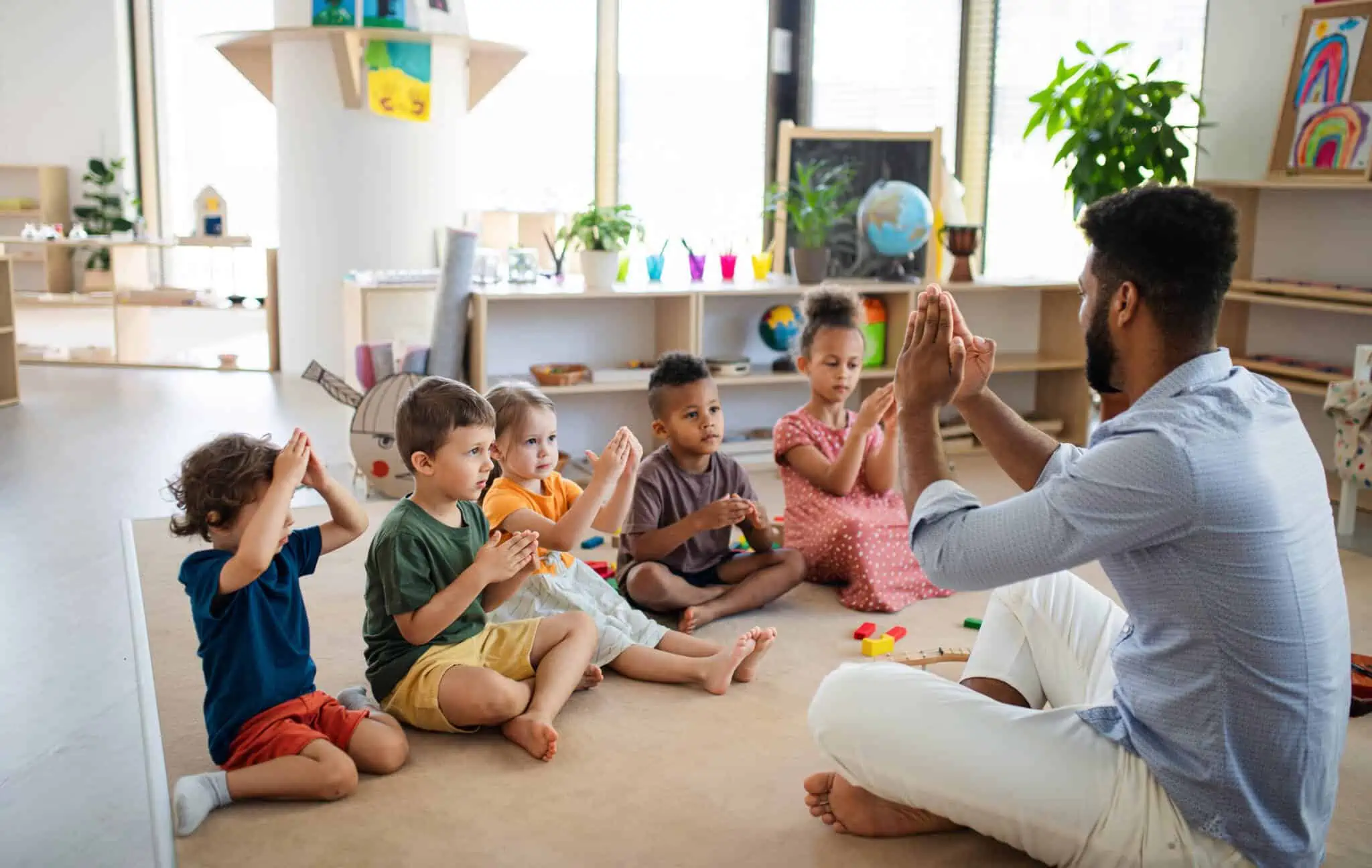 Programa Creche Feliz: Como funciona e a quem se destina grupo de crianças pequenas no infantario, no ambito do programa creche feliz, sentadas no chão a trabalhar com o monitor