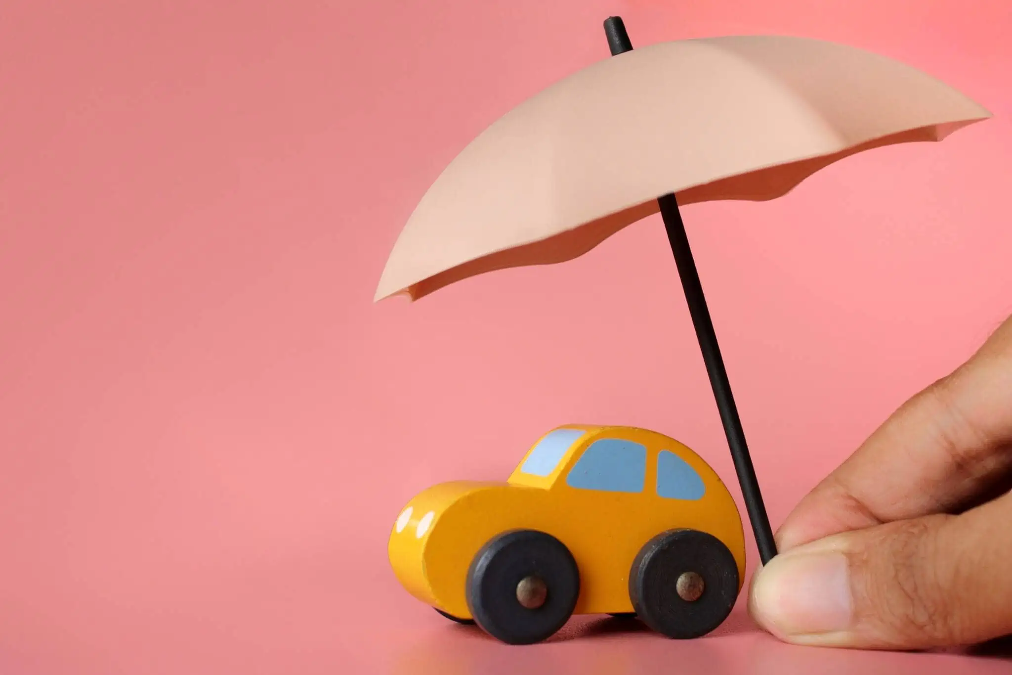 produção fotográfica com um pequeno carro amarelo brinquedo sob um chapéu sol segurado por uma mão ilustram a contratação de um seguro automóvel por dias